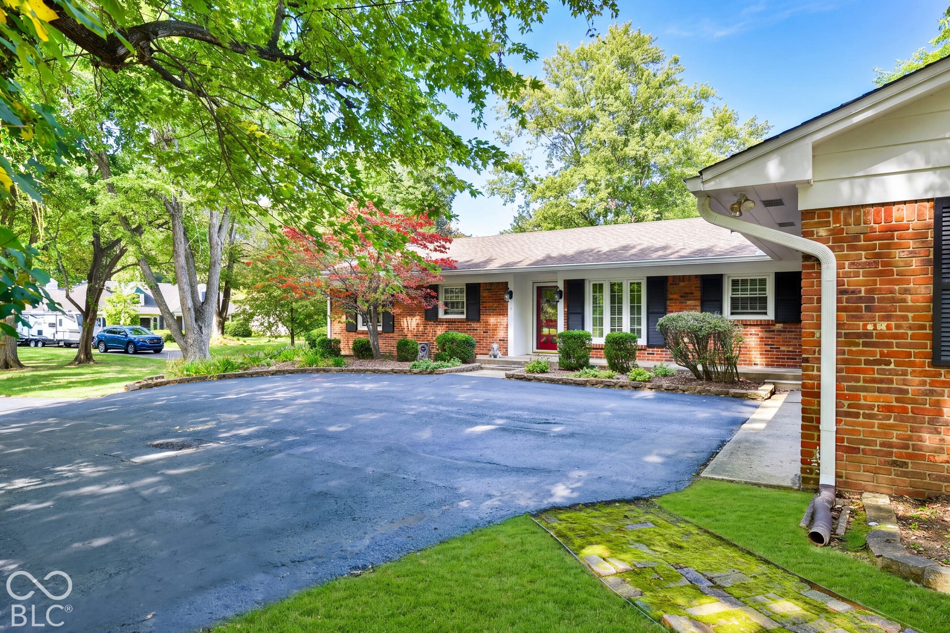 Single-story exterior featuring a brick facade, asphalt driveway, shuttered windows, and mature landscaping