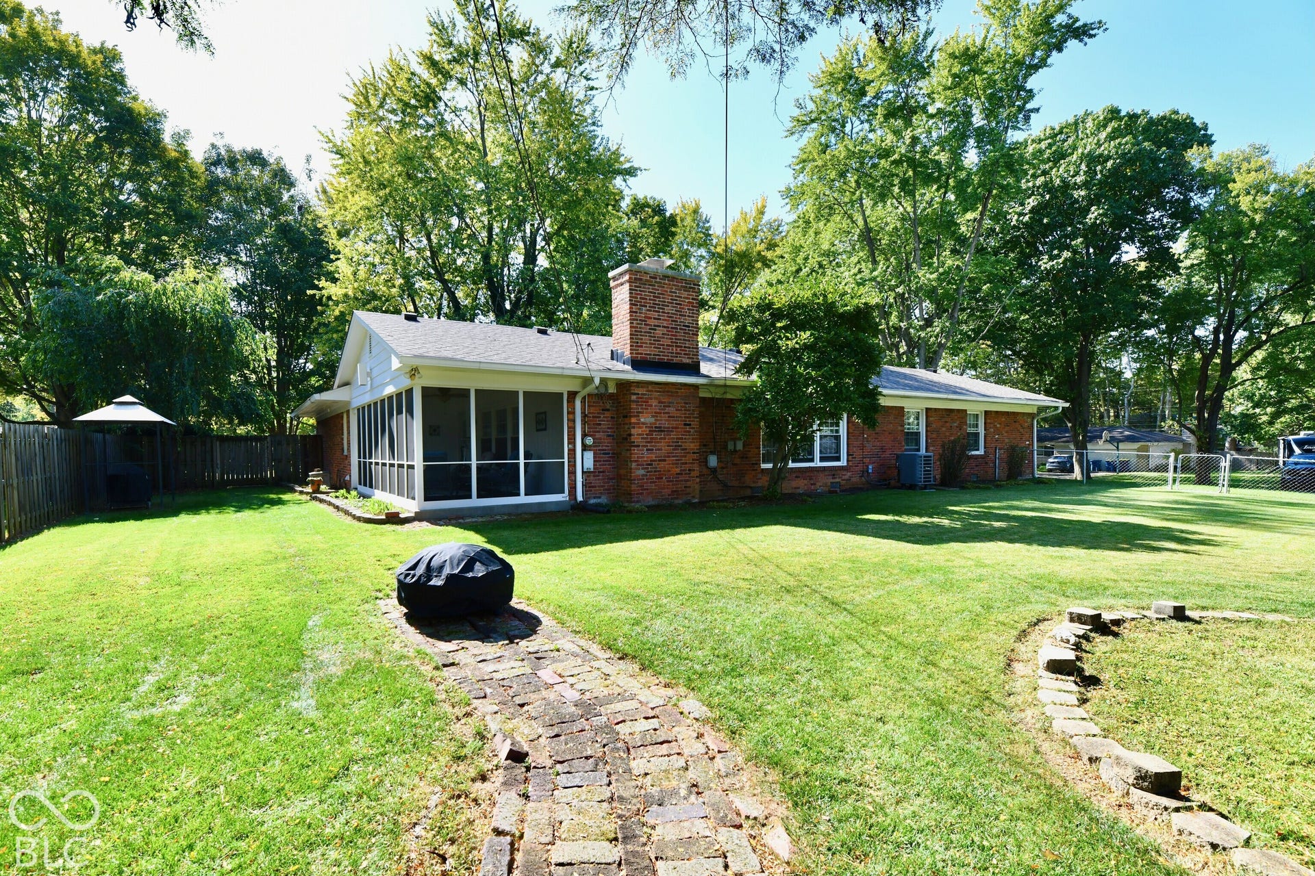 Brick exterior residence featuring a screened-in porch, a central brick chimney, a stone paver walkway, and a spacious backyard with mature trees