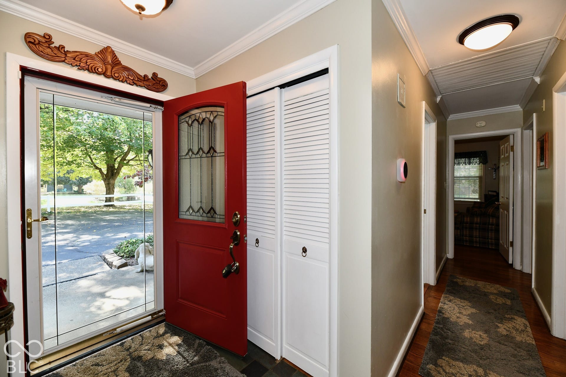 Entryway featuring a solid wood door with a stained-glass insert, louvered bi-fold closet doors, crown molding, and flush-mount ceiling lighting