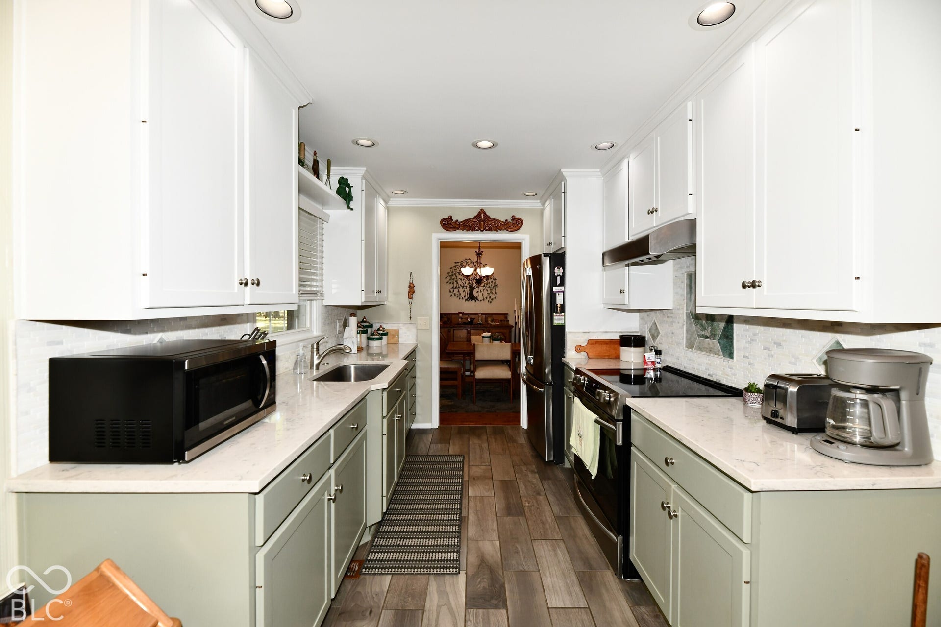 Kitchen featuring two-tone cabinetry with white upper and sage lower units, quartz countertops, tile backsplash, stainless steel sink, and wood-finish flooring