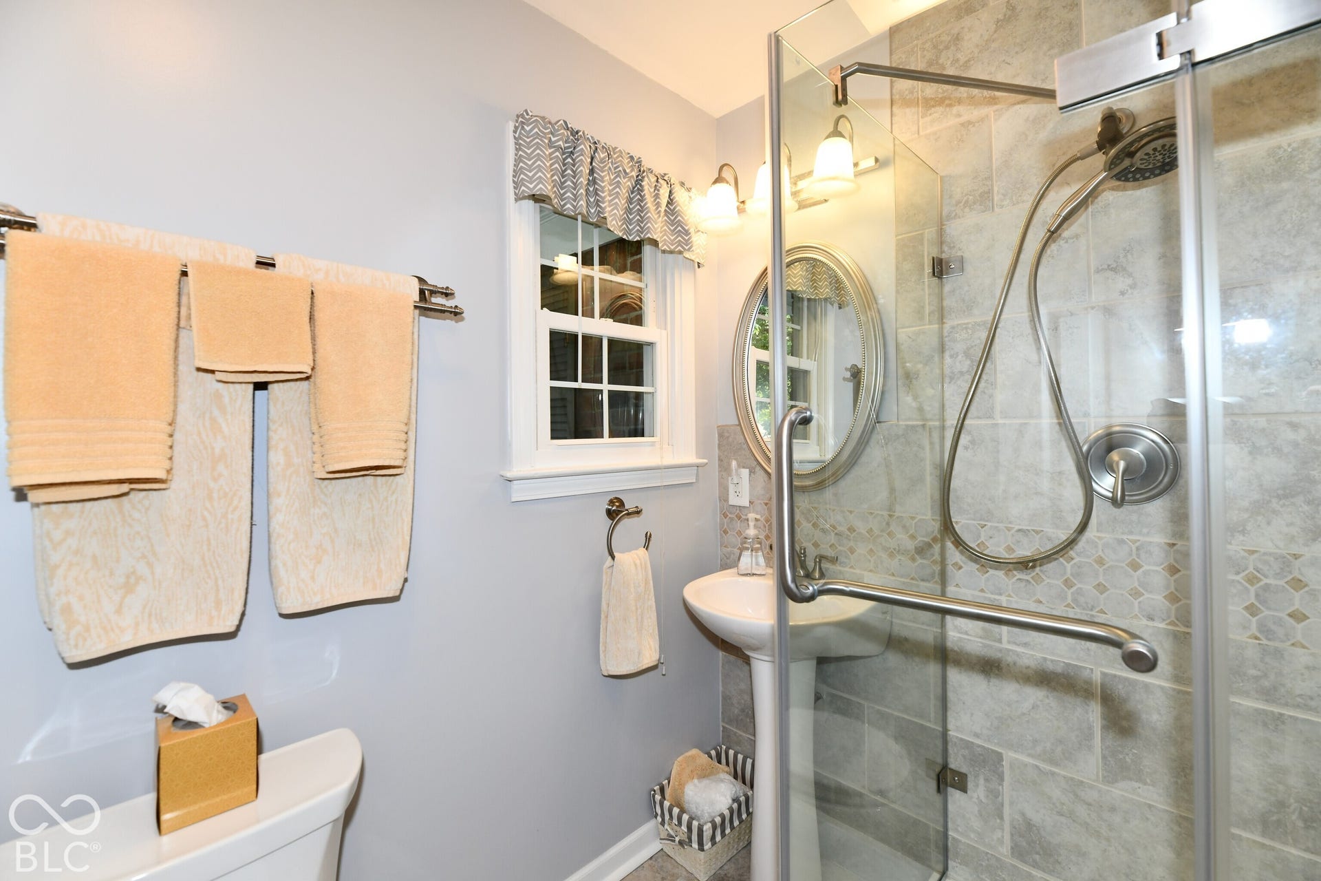 Bathroom featuring a glass-enclosed shower with tiled walls, a pedestal sink, a wall-mounted oval mirror, and a multi-light fixture