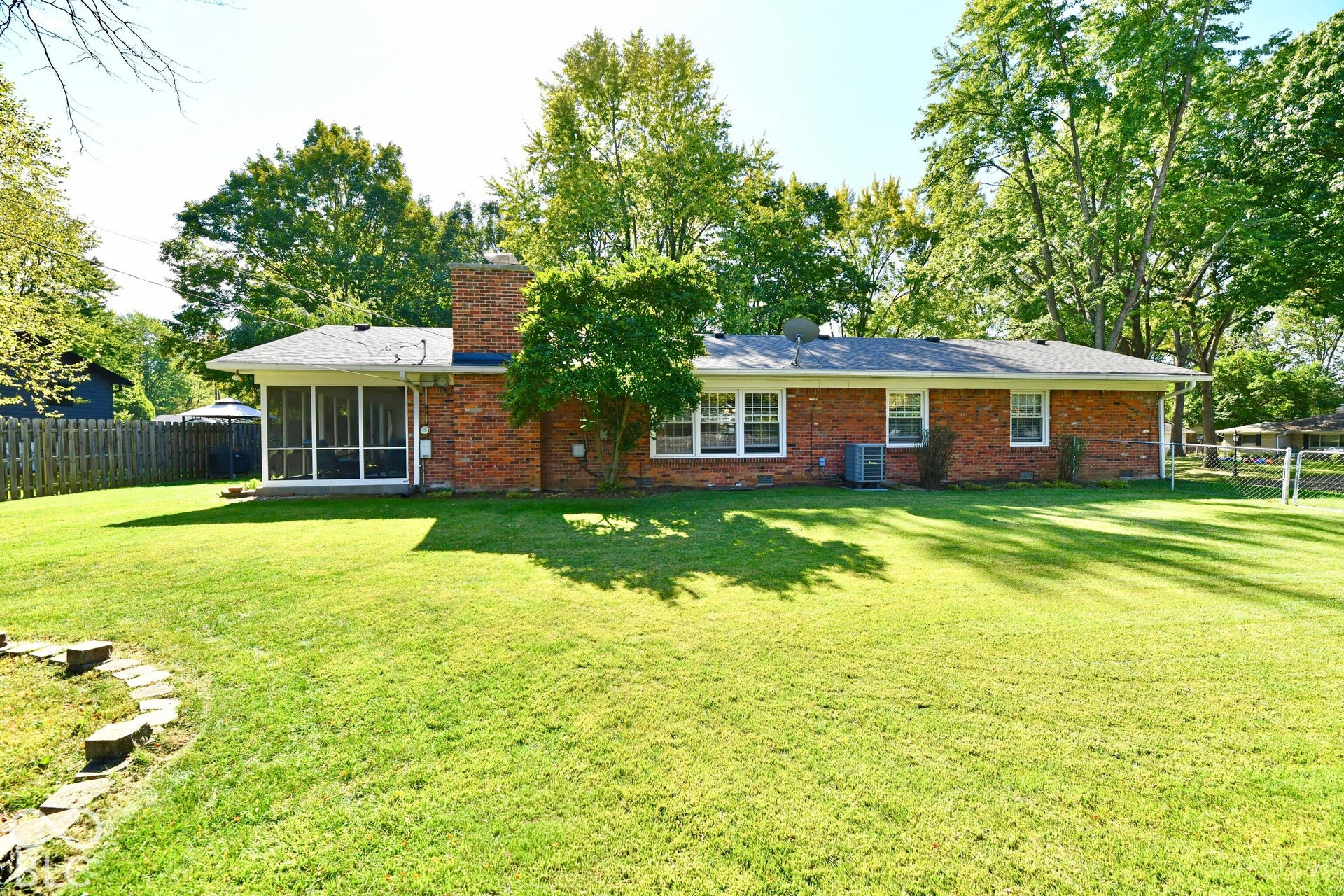 Exterior brick facade featuring a screened-in porch, masonry chimney, expansive lawn, and partial wood fencing