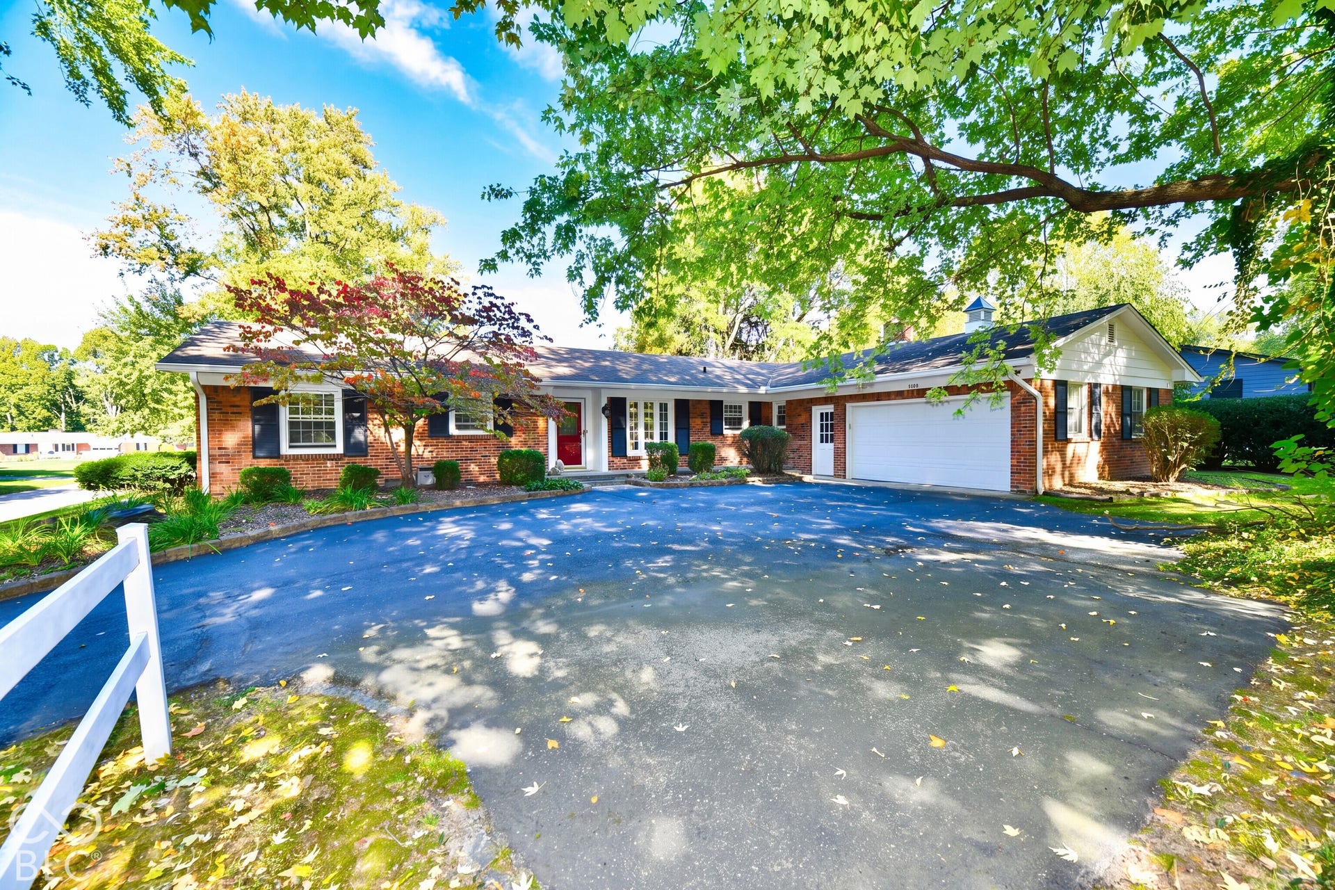 Single-story brick exterior featuring a white attached two-car garage, dark decorative shutters, and an expansive asphalt driveway