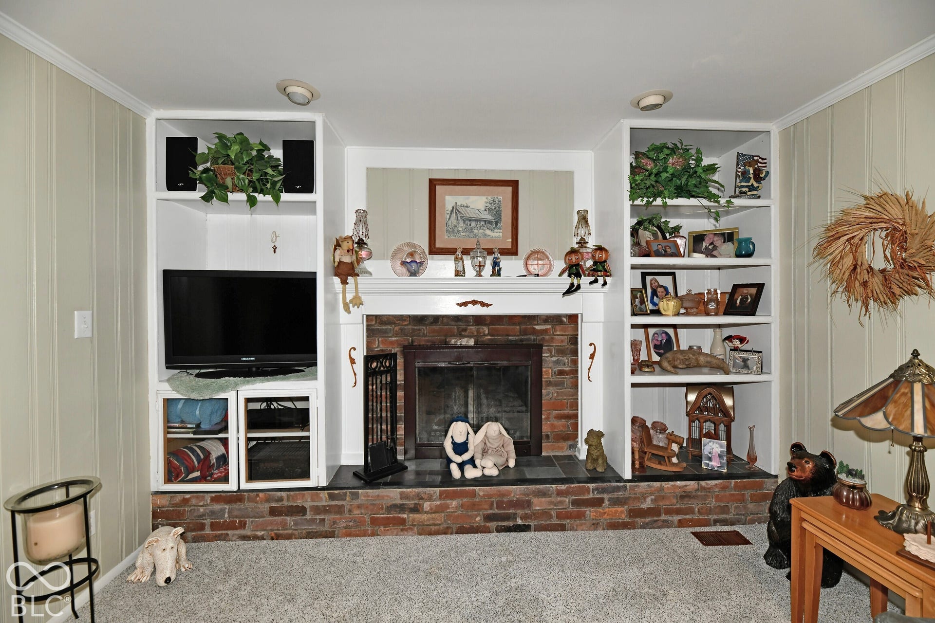 Brick fireplace featuring a raised hearth, white mantel, and integrated floor-to-ceiling built-in cabinetry with shelving