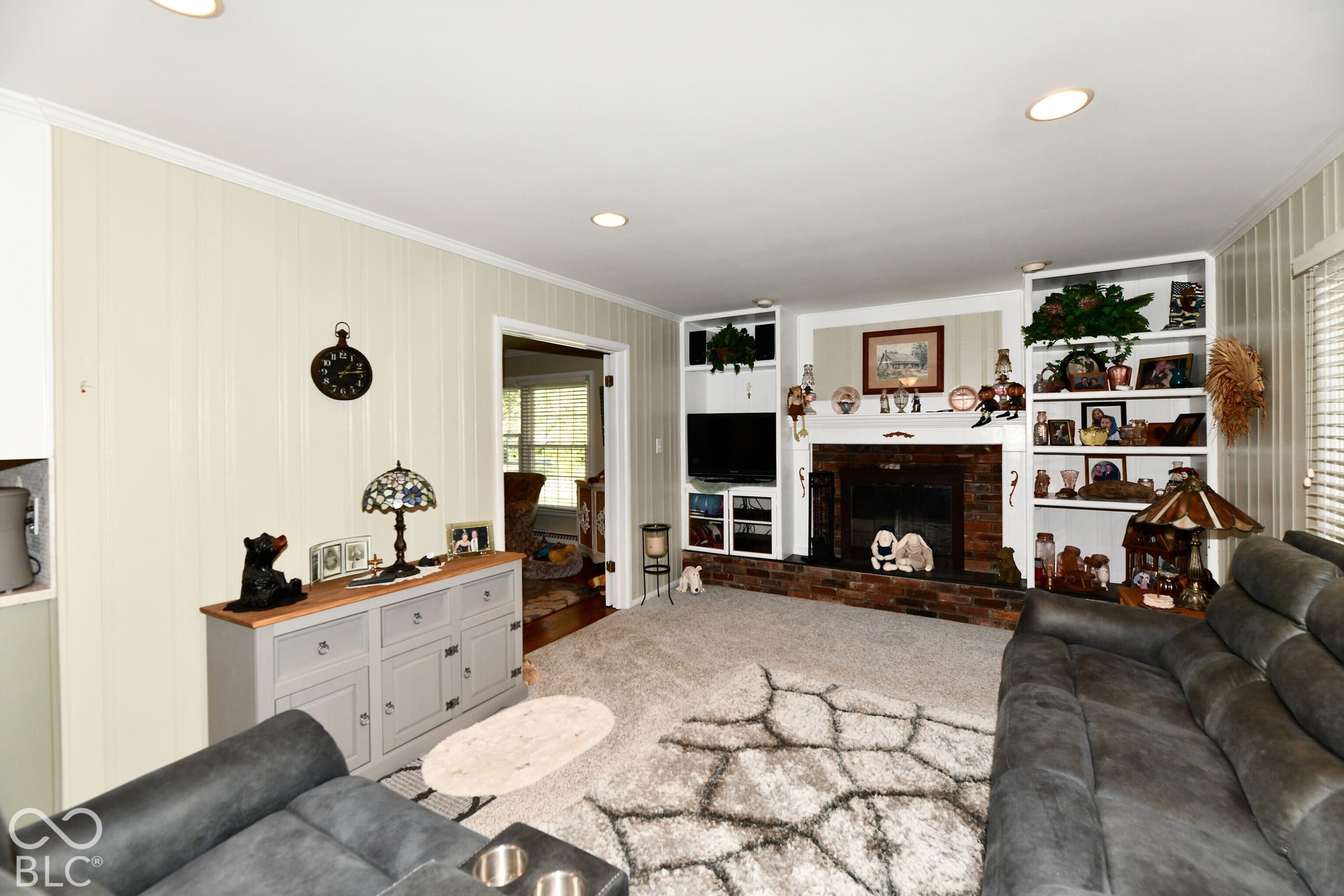 Living area featuring a brick fireplace, built-in shelving, recessed lighting, and vertical paneling