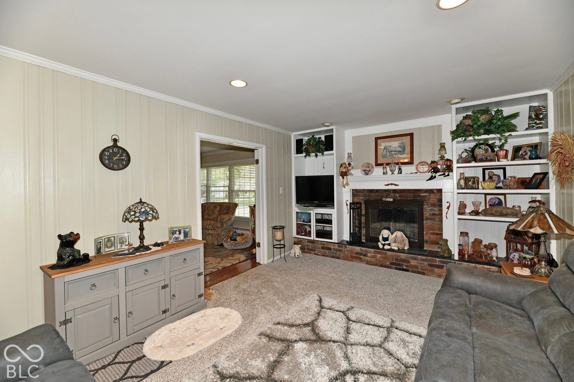 Interior space featuring a brick-surround fireplace, built-in floor-to-ceiling shelving, recessed lighting, and vertical paneled wall detailing