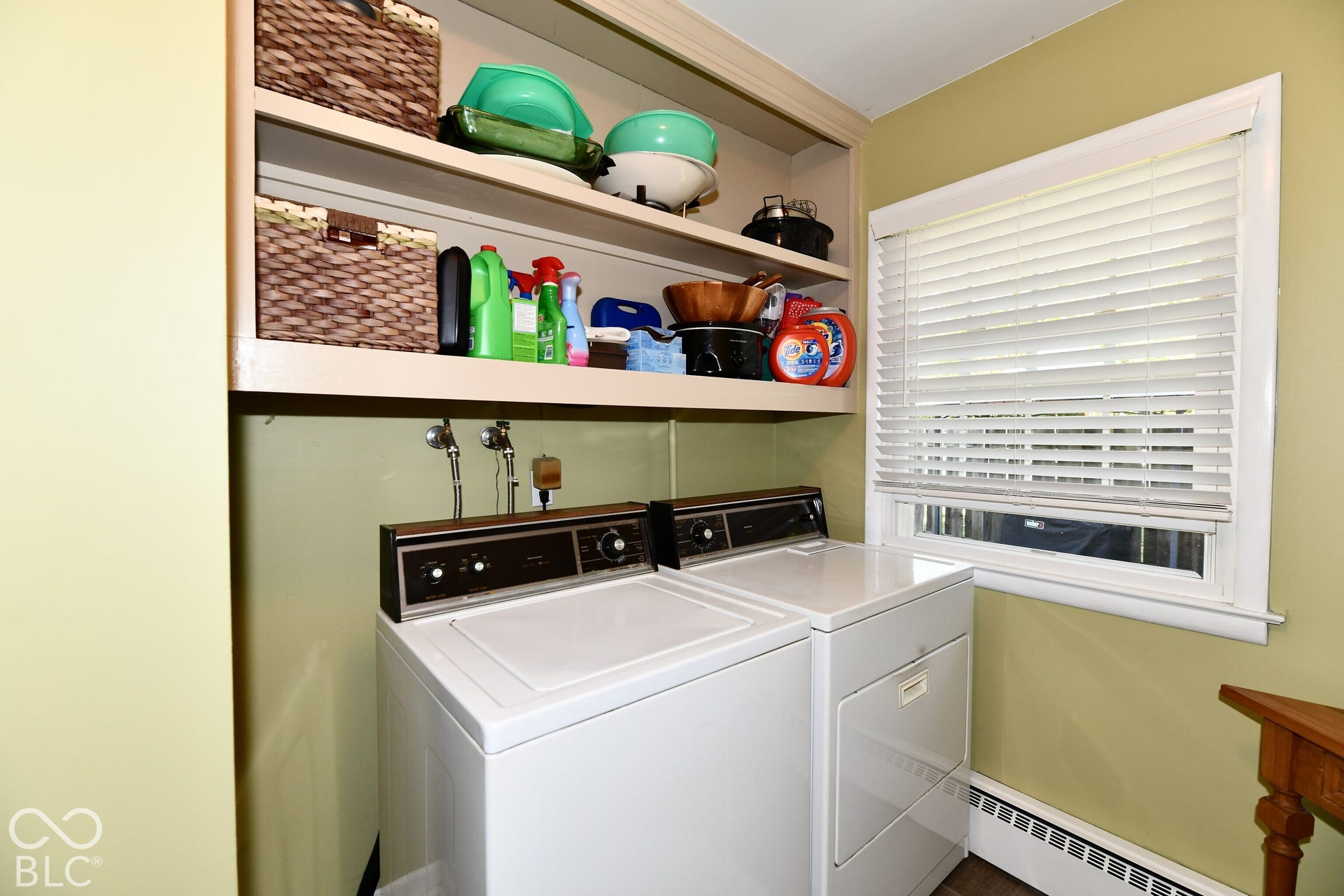 Laundry space featuring built-in overhead storage shelving and a window with horizontal blinds