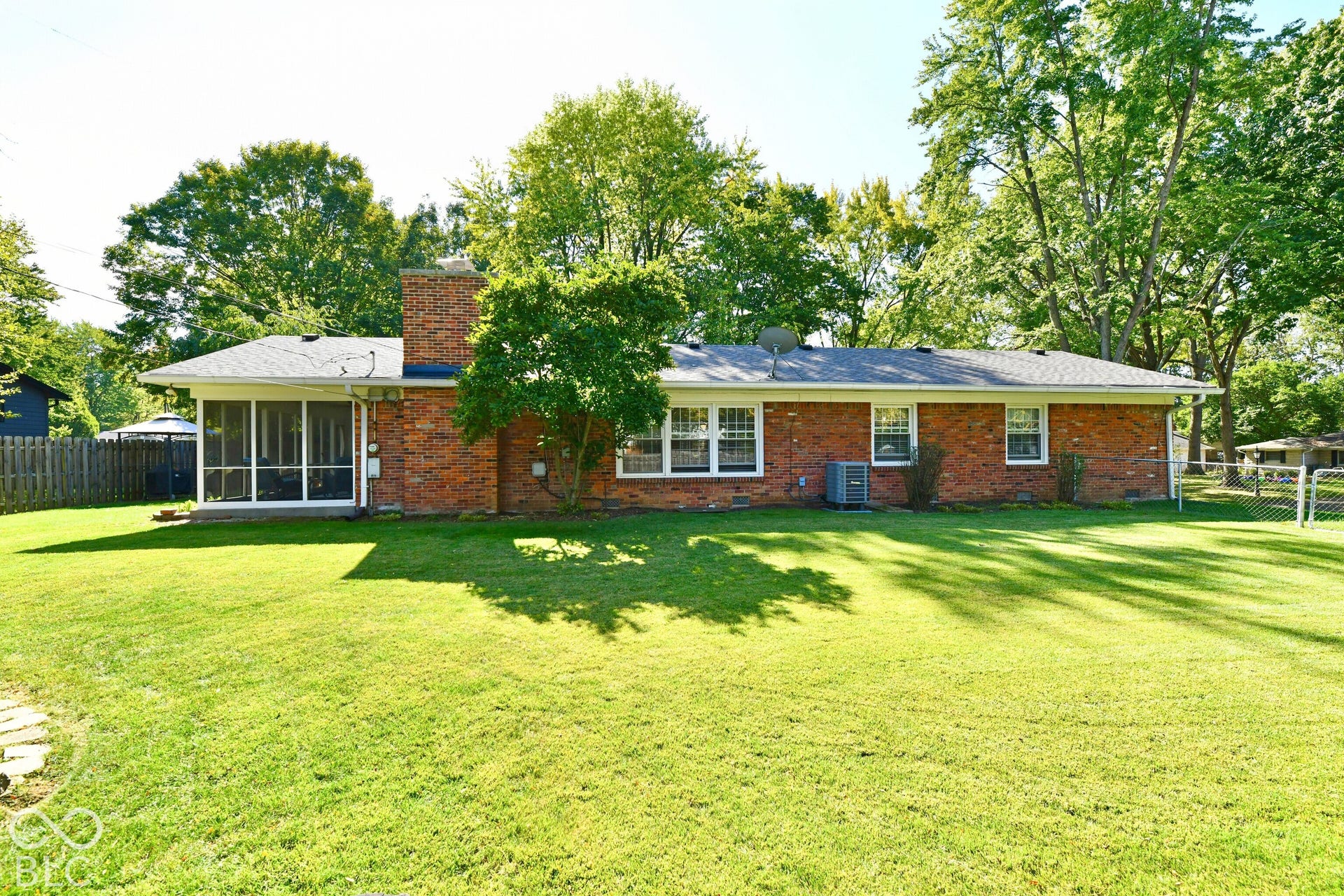 Single-story brick exterior featuring a rear screened-in porch, a prominent brick chimney, multi-pane windows, and a expansive lawn with mature trees