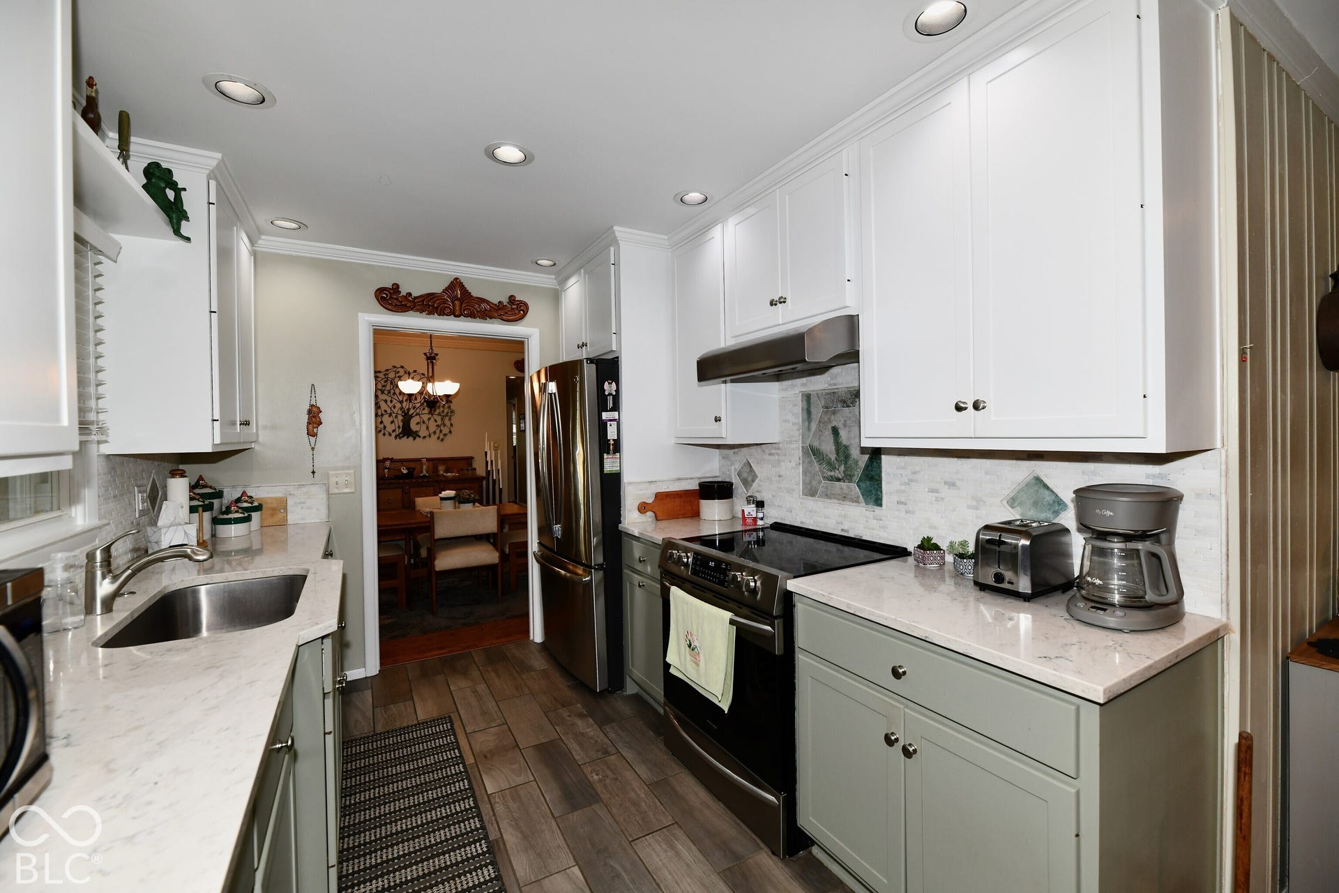 Kitchen featuring white upper cabinetry, sage green lower cabinetry, stone-finish countertops, stainless steel appliances, and wood-finish flooring