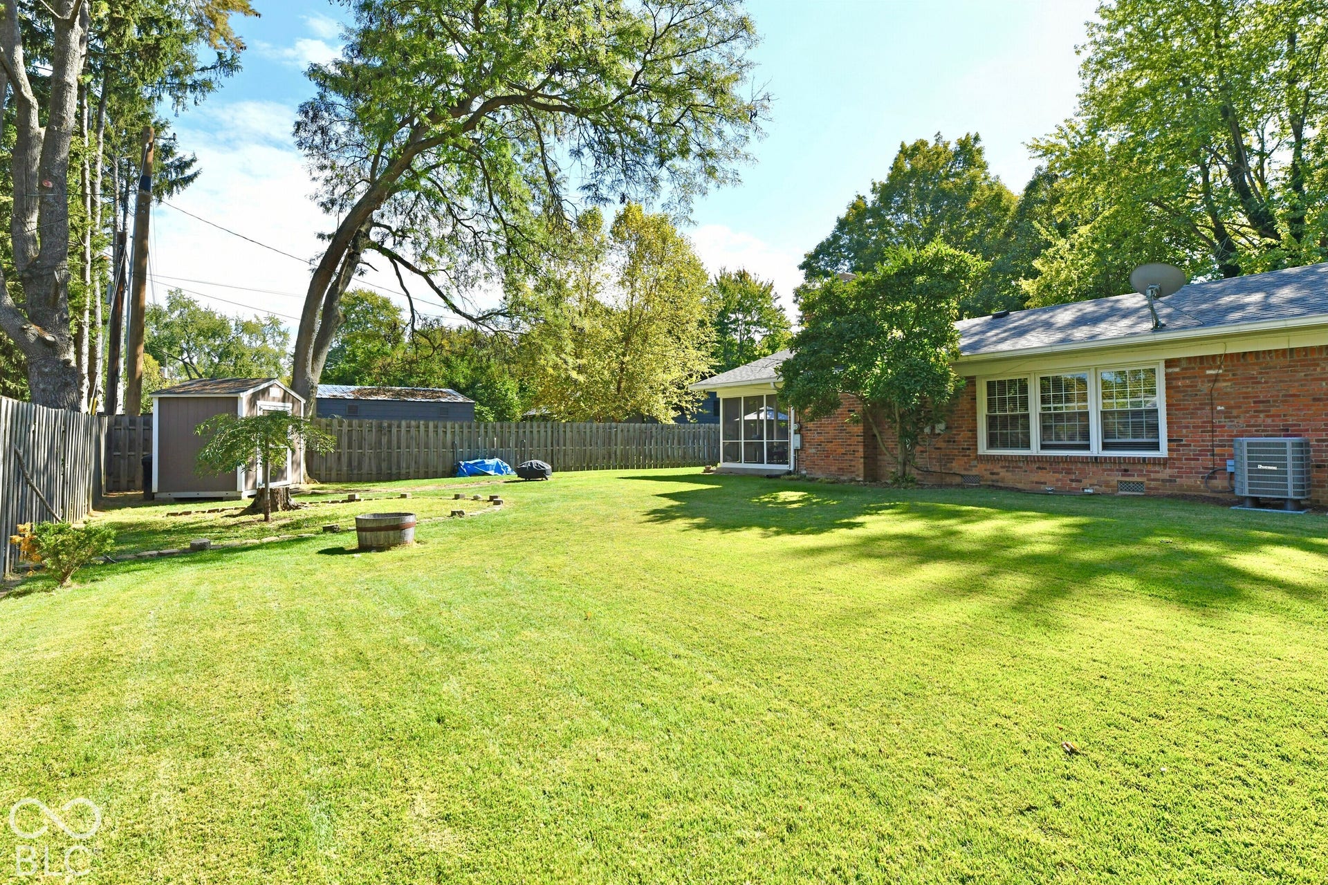 Backyard featuring a red brick exterior, fenced perimeter, mature trees, lawn, and an exterior storage structure