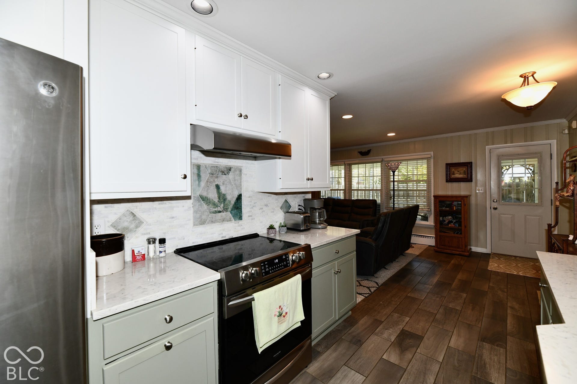 Kitchen featuring custom white upper and sage green lower cabinetry, quartz countertops, a decorative tile backsplash, stainless steel range with overhead vent, and wood-finish flooring