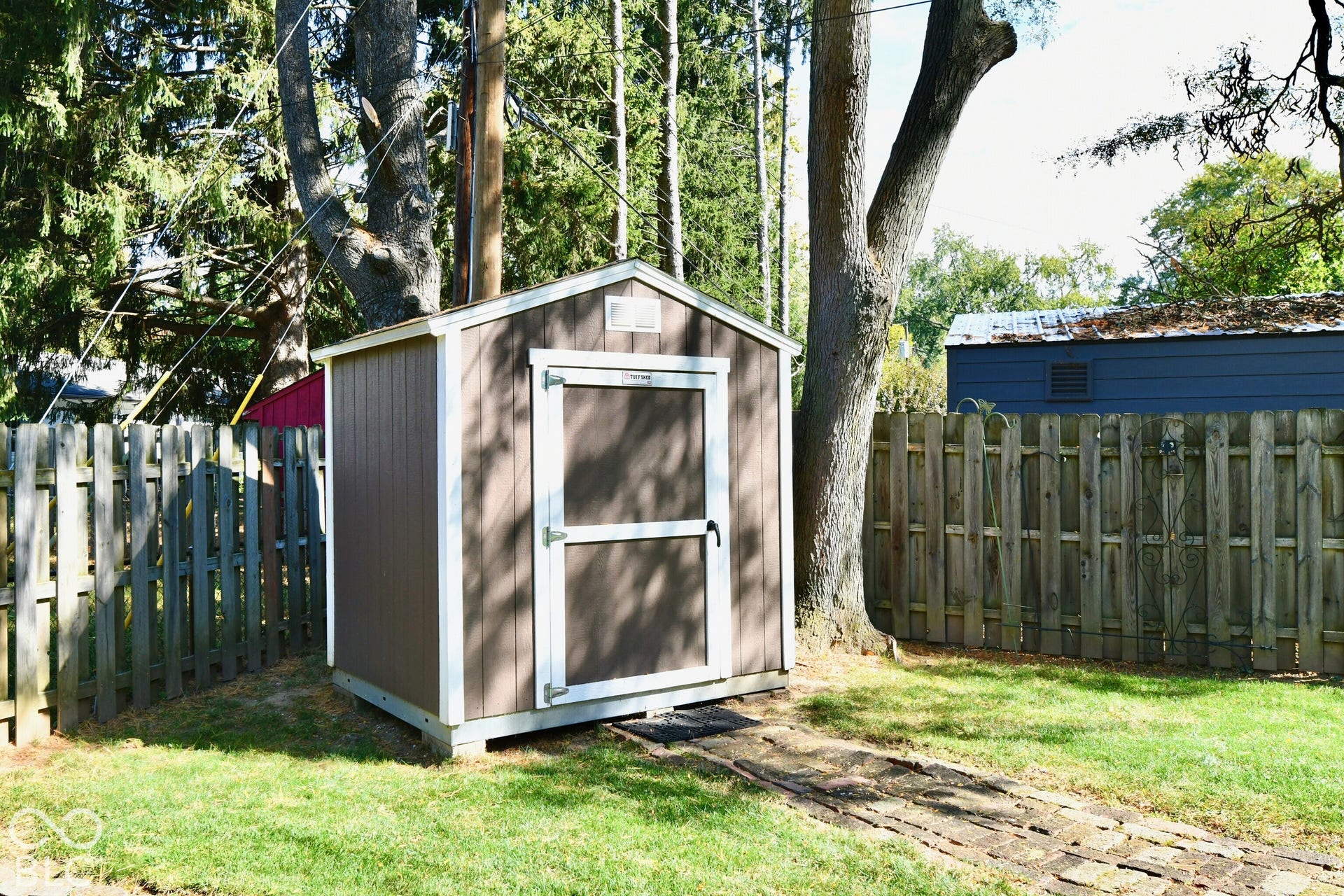 Detached storage structure featuring vertical siding, white trim, a gabled roof, and a stone paver path
