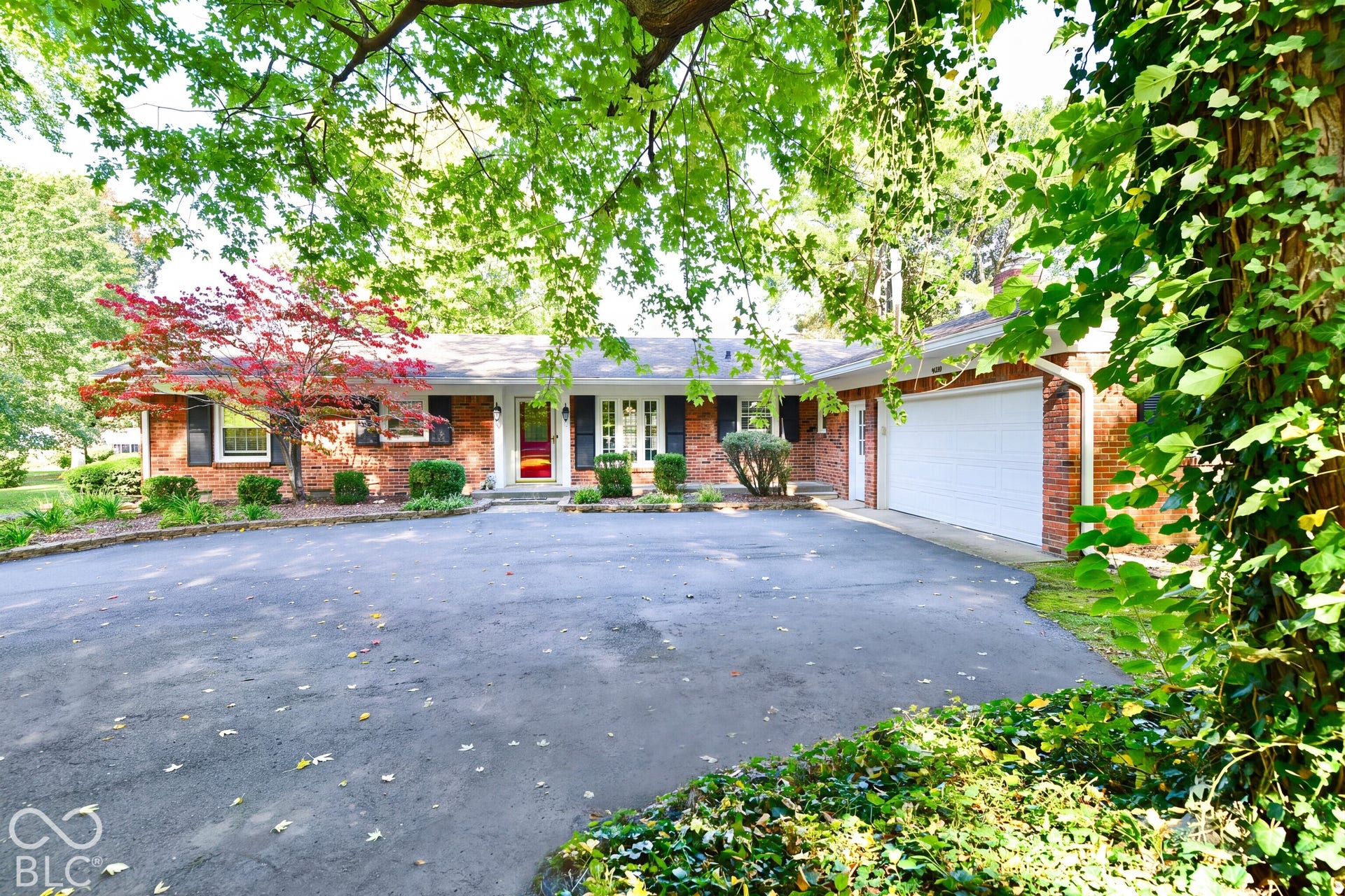 Single-story brick exterior featuring a multi-car attached garage, expansive asphalt driveway, decorative window shutters, and established landscaping