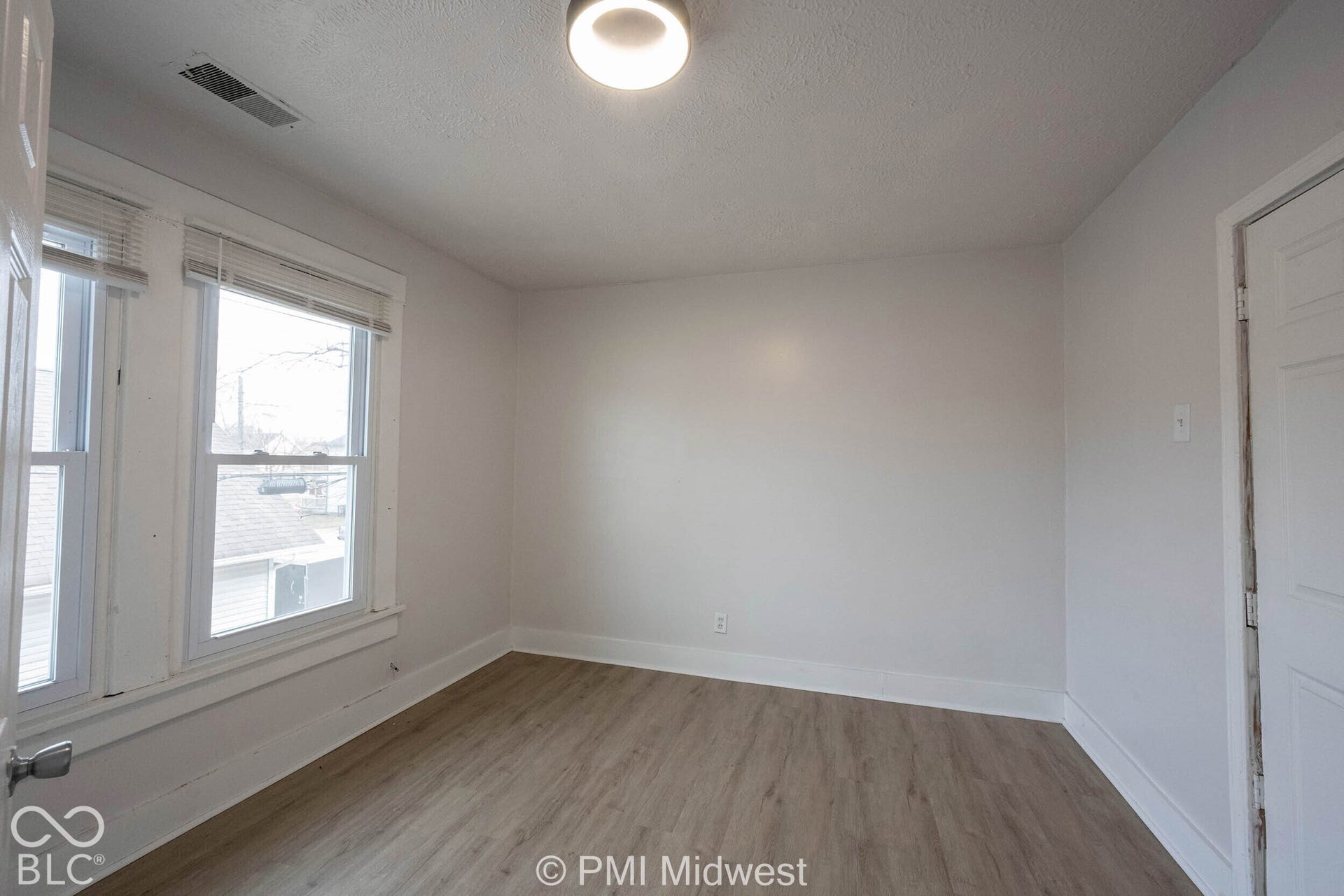 Interior space featuring wood-finish flooring, neutral wall tones, dual windows, and a flush-mount light fixture