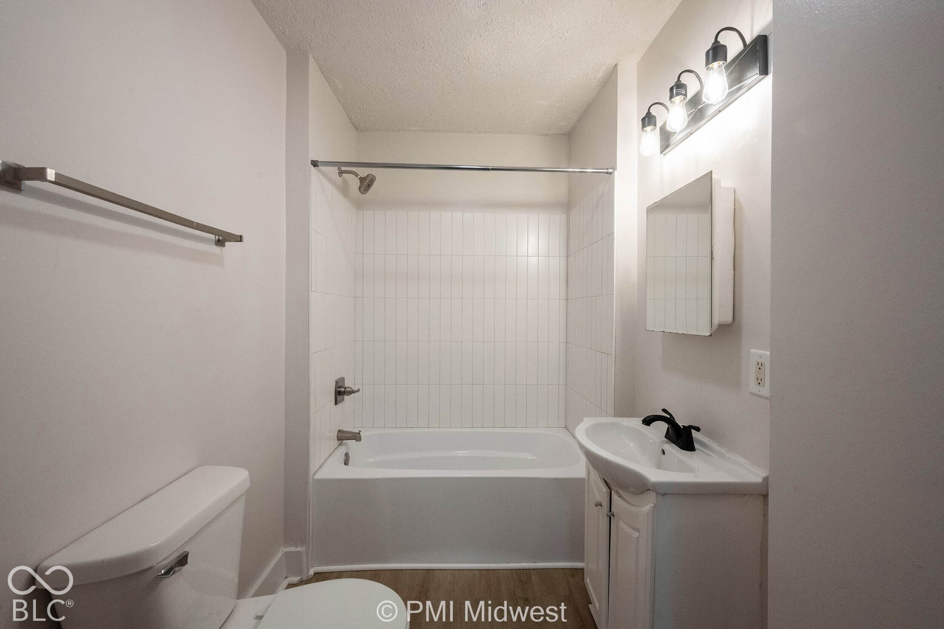 Full bathroom featuring a tub-shower combination with vertical white wall tile, a vanity with a white basin and dark hardware, a surface-mounted medicine cabinet, and three-light vanity fixture