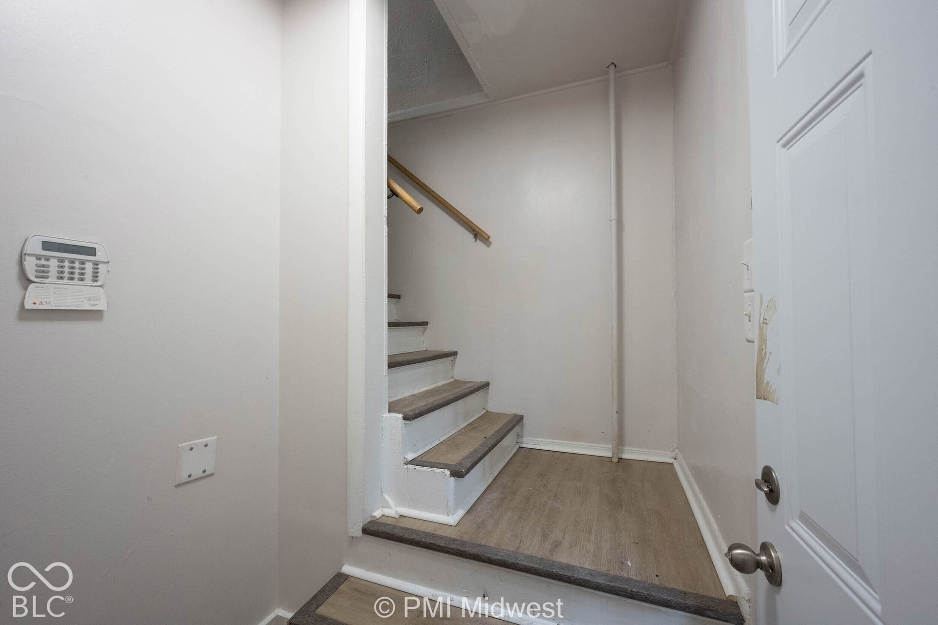 Interior staircase featuring wood-finish treads, white risers, a mounted handrail, and an integrated security system wall panel