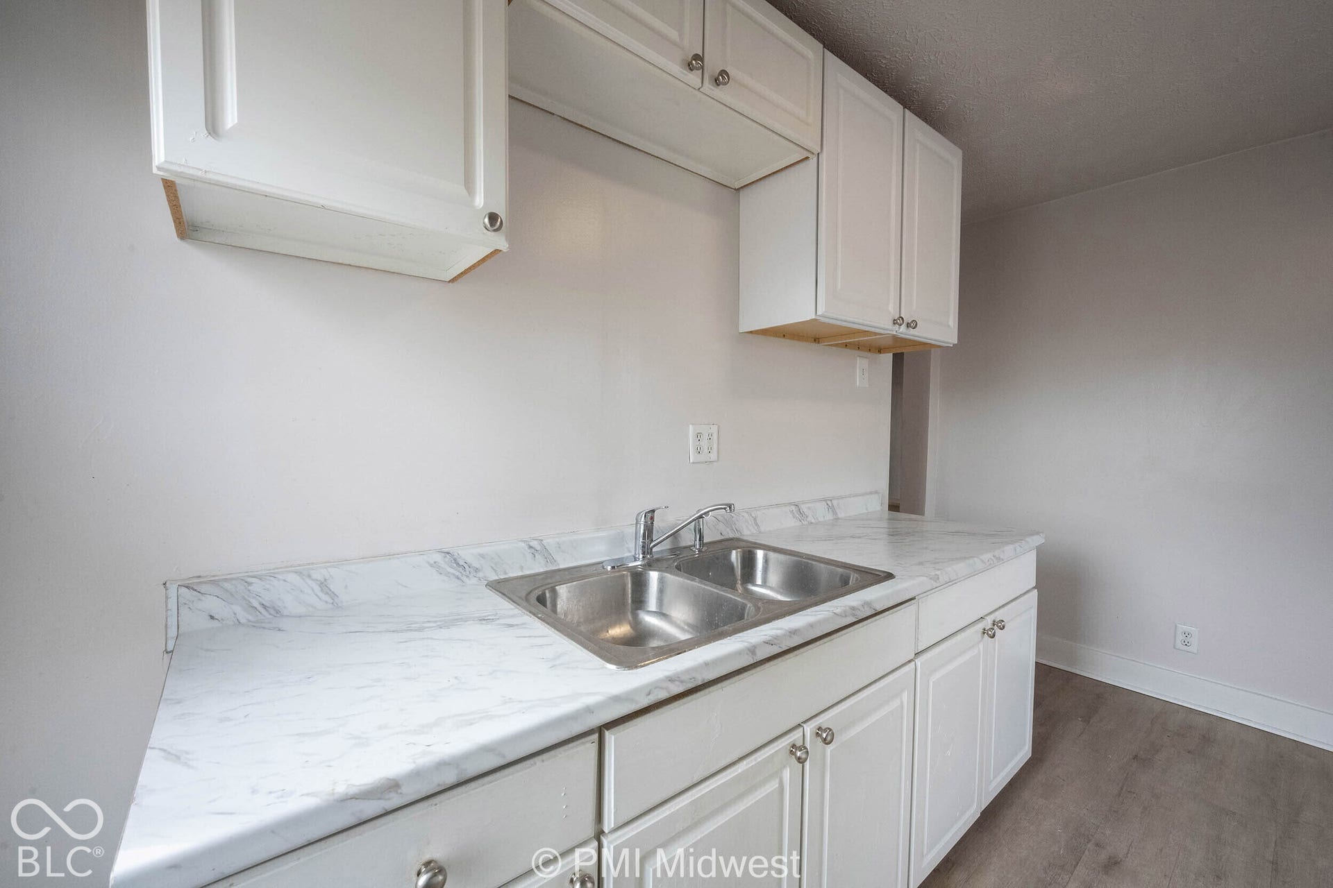 White cabinetry, double-basin stainless steel sink, chrome faucet, stone-finish laminate countertop, and wood-finish flooring