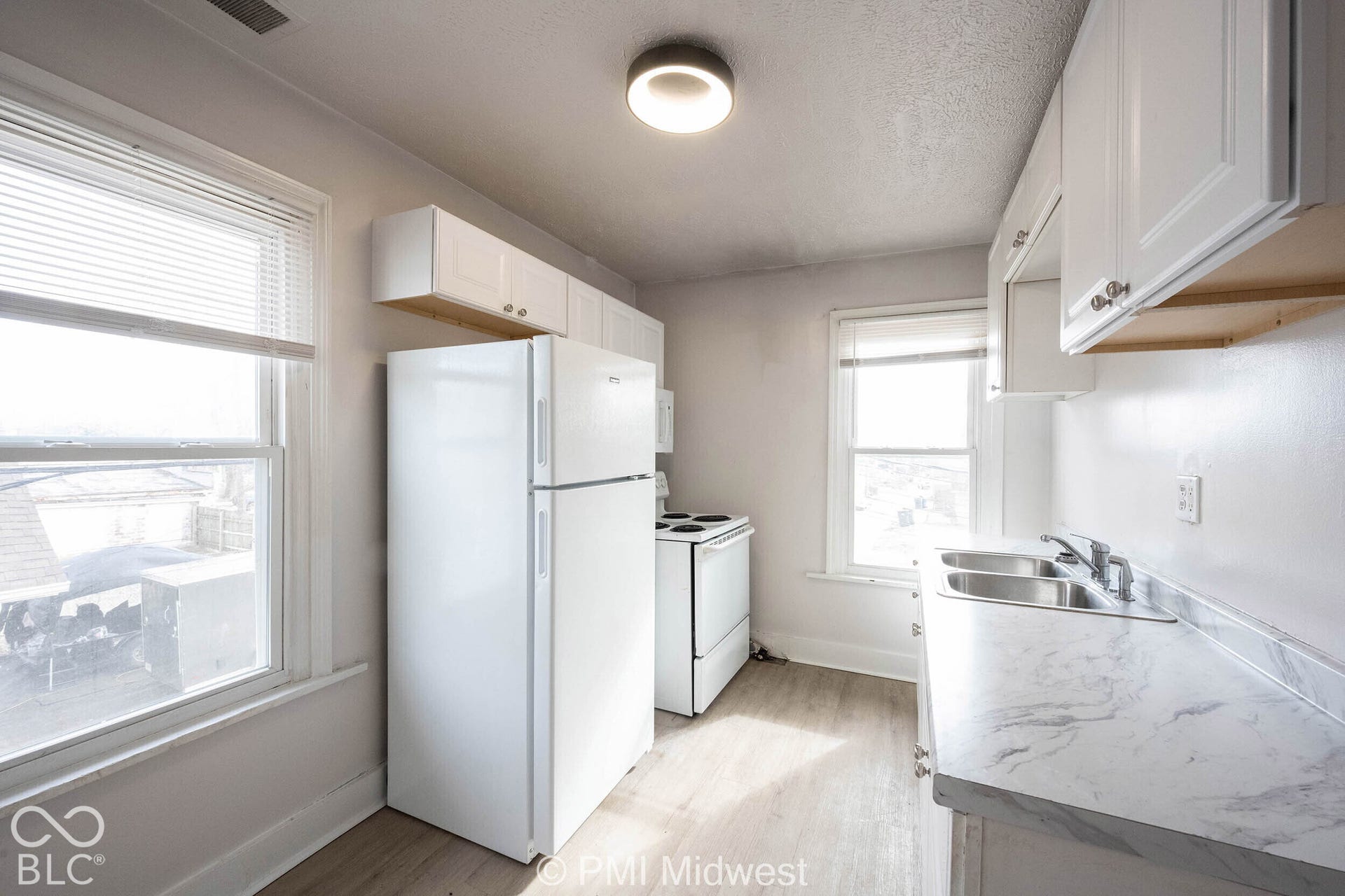 Kitchen featuring white cabinetry, wood-finish flooring, dual-basin stainless steel sink, and marble-patterned countertops