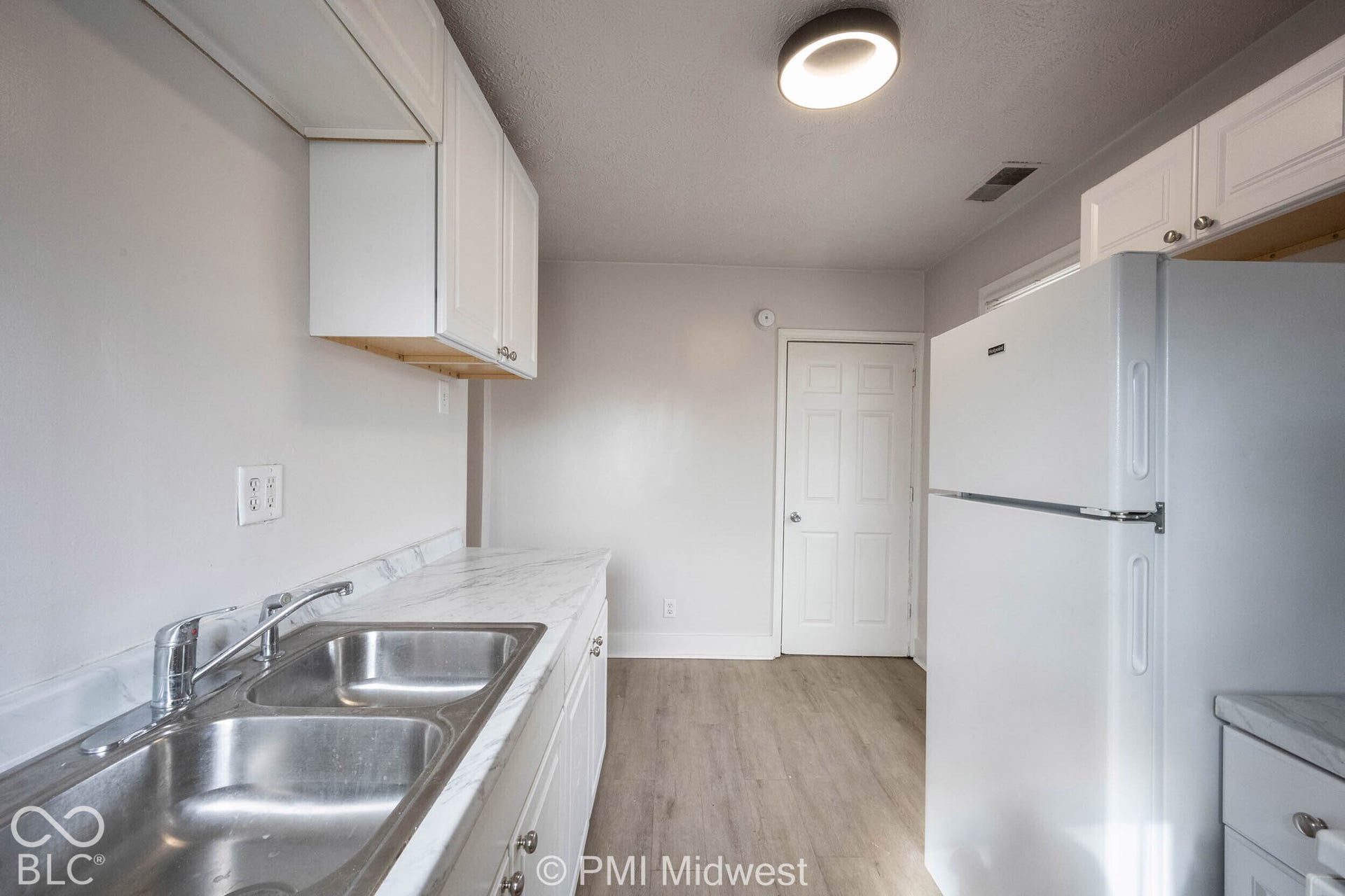 Kitchen featuring white cabinetry, stone-patterned countertops, a double-basin stainless steel sink with a high-arch faucet, and wood-finish flooring