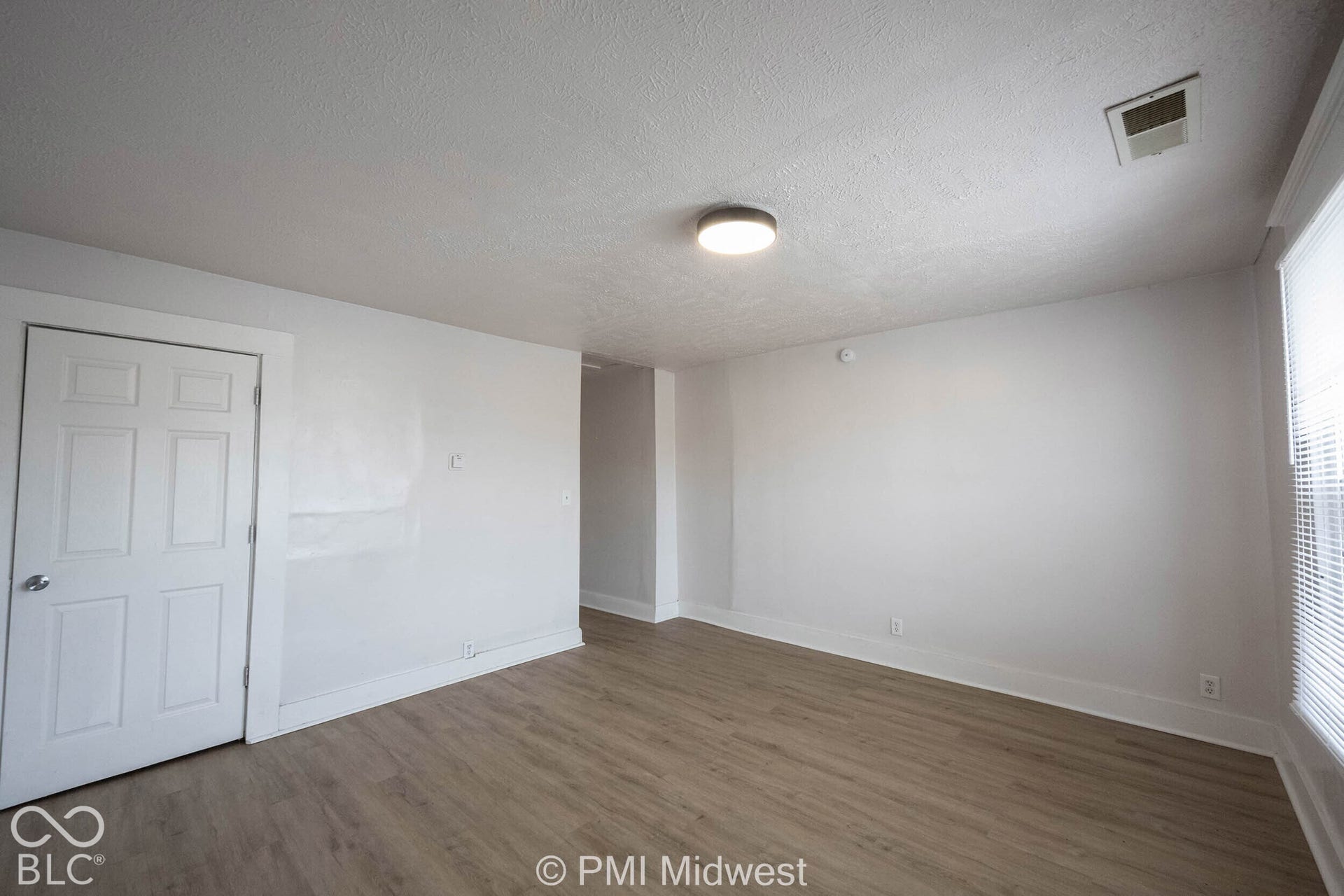 Interior room featuring wood-finish flooring, a six-panel door, neutral wall paint, and a central flush-mount ceiling light