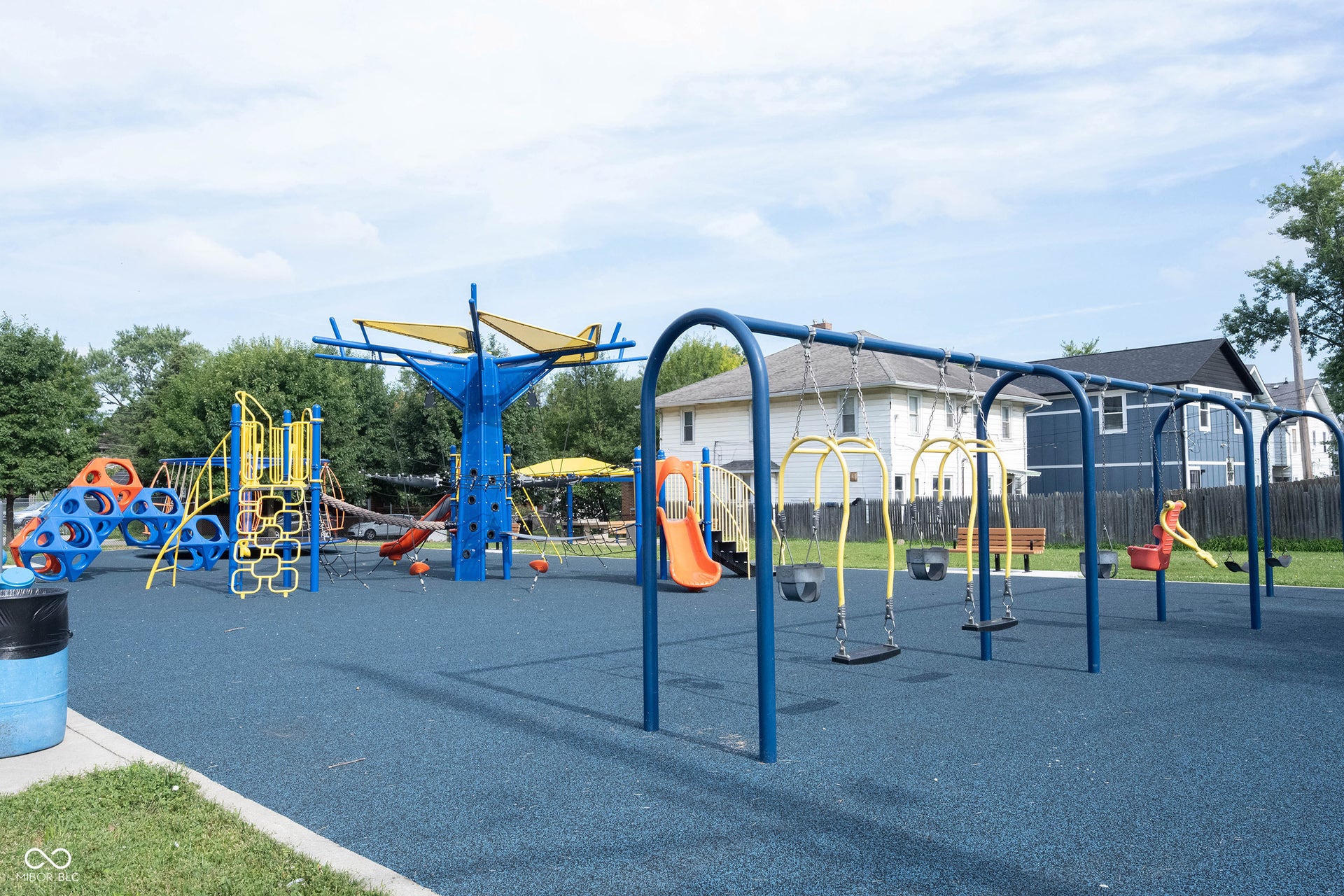 Spacious playground featuring diverse play structures, multiple swing sets, a resilient rubberized surface, sun shades, and perimeter fencing