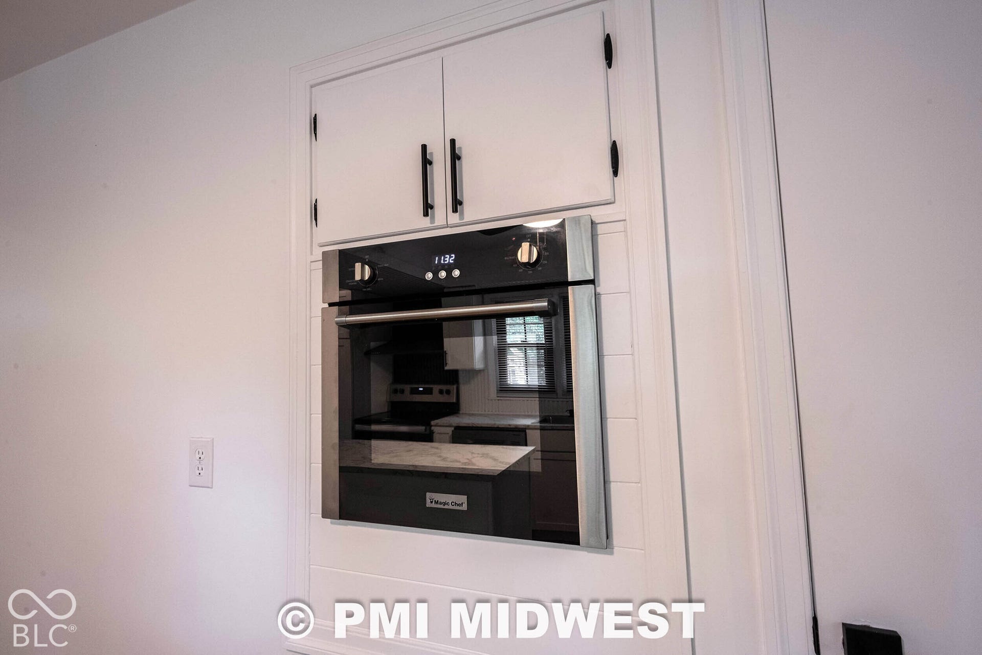 Built-in stainless steel wall oven, recessed white cabinetry with matte black hardware, and white shiplap detailing