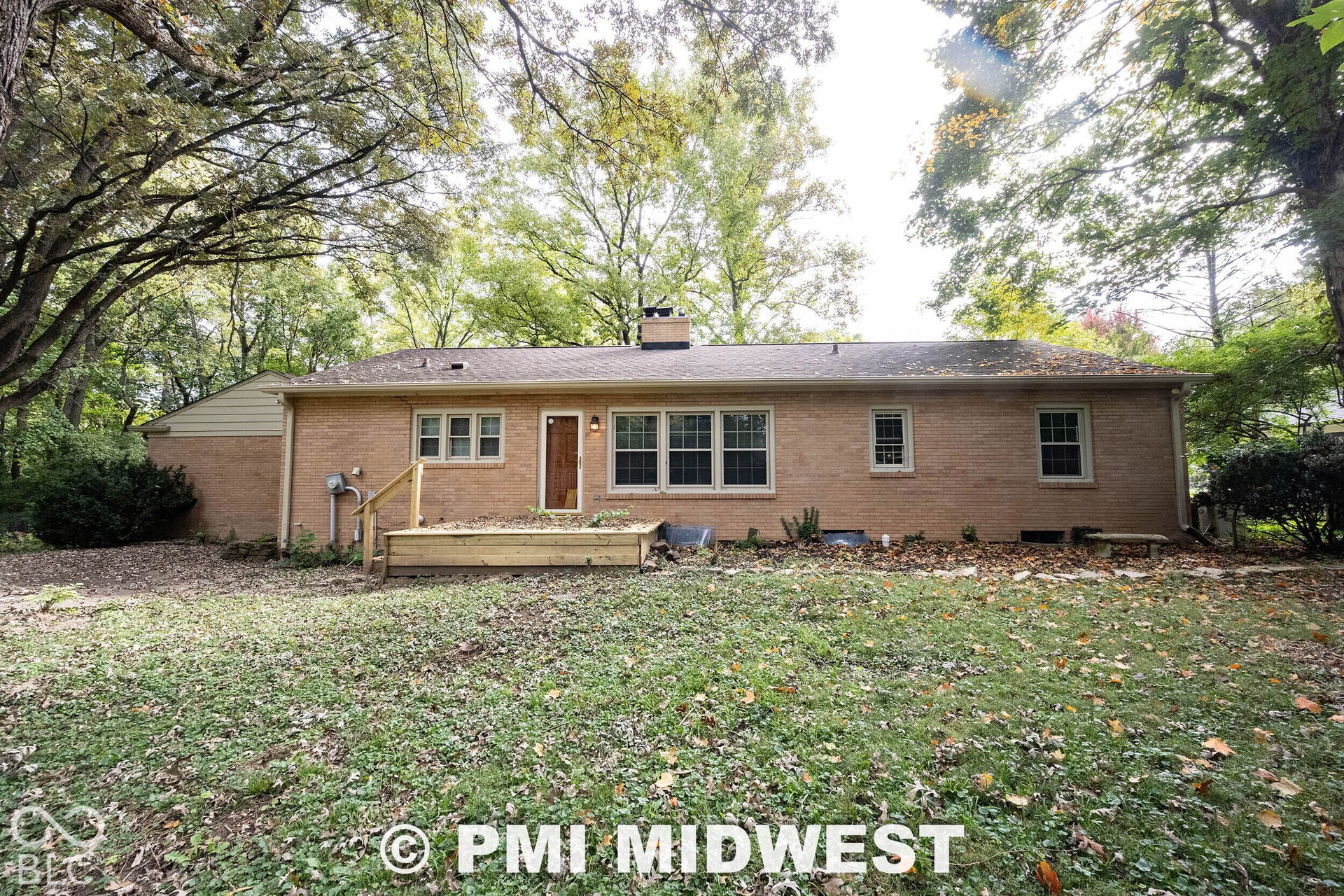 Brick exterior residence featuring a wooden deck, a chimney, and mature trees on the surrounding grounds