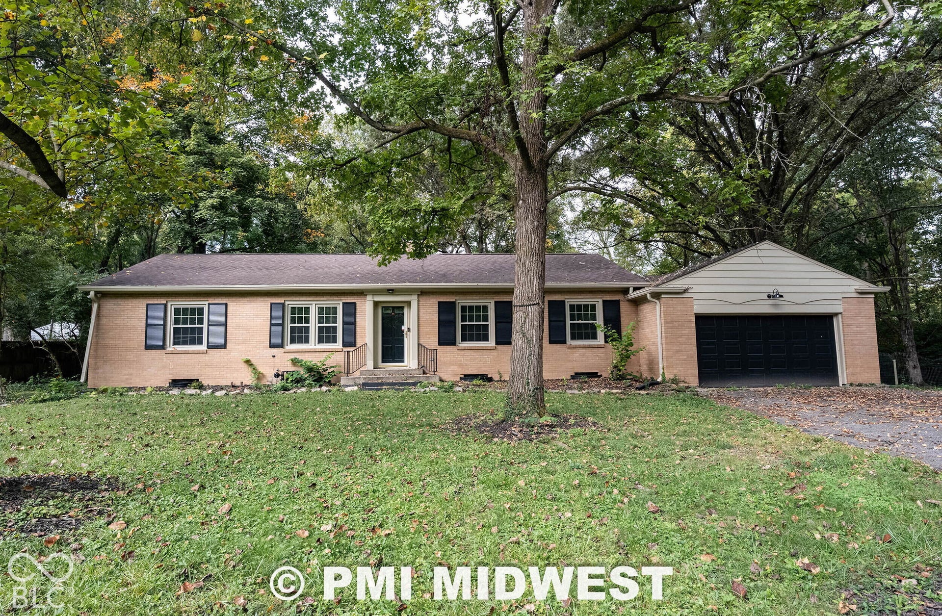 Single-story brick exterior featuring dark shutters, attached garage, and mature trees on the lot