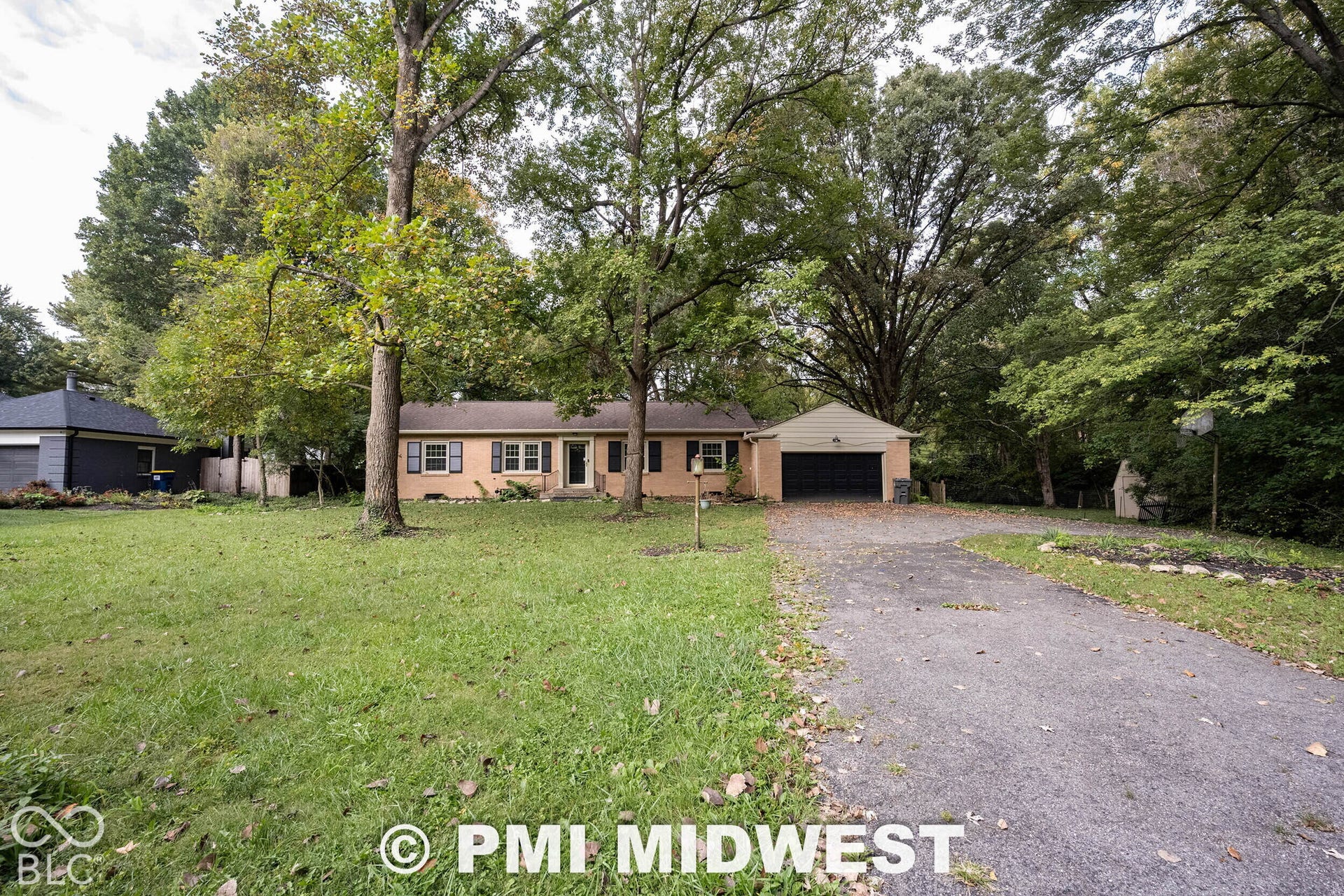 Single-story residence with a brick exterior, shutter-framed windows, attached garage, and mature trees on a spacious lot