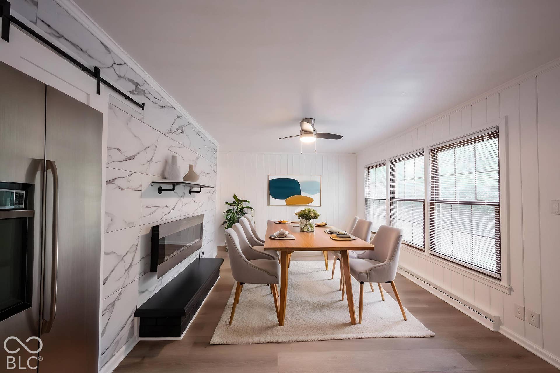 Stone-finish wall cladding with integrated wall-mounted fireplace and black shelving, vertical wood wall paneling, stainless steel refrigerator, and wood-finish flooring