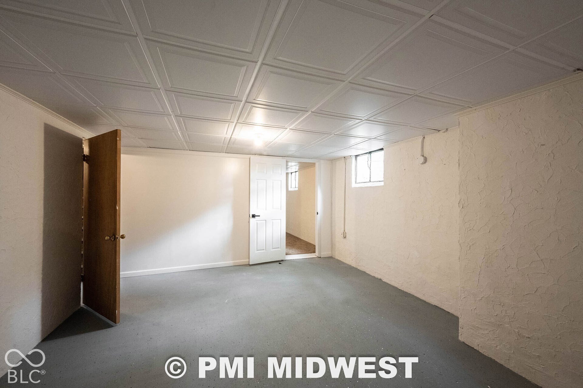 Finished interior space featuring a coffered-style drop ceiling, painted masonry walls, painted flooring, and a six-panel door
