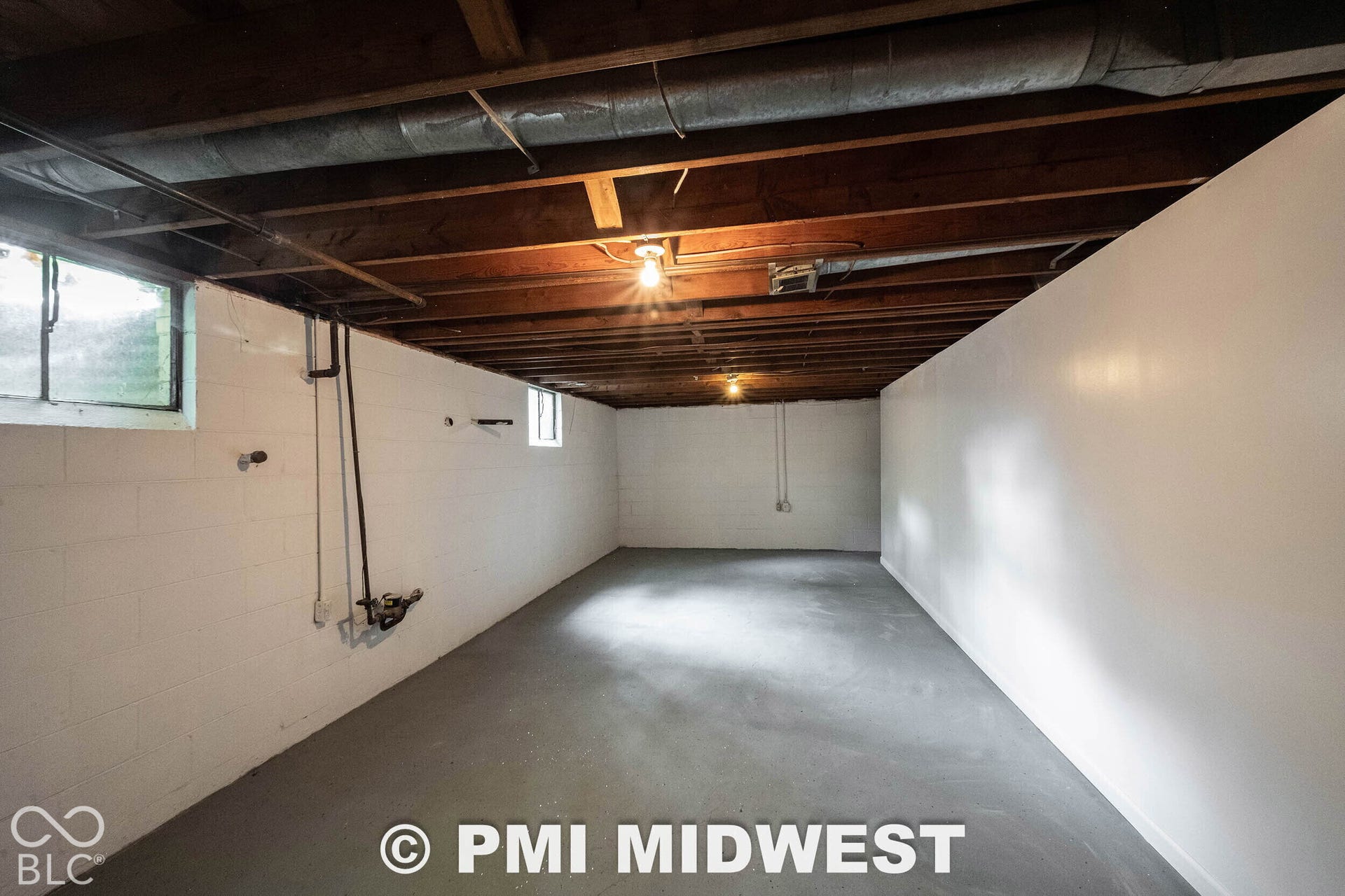 Unfinished space featuring painted concrete masonry unit walls, a painted concrete floor, and exposed timber joist ceiling