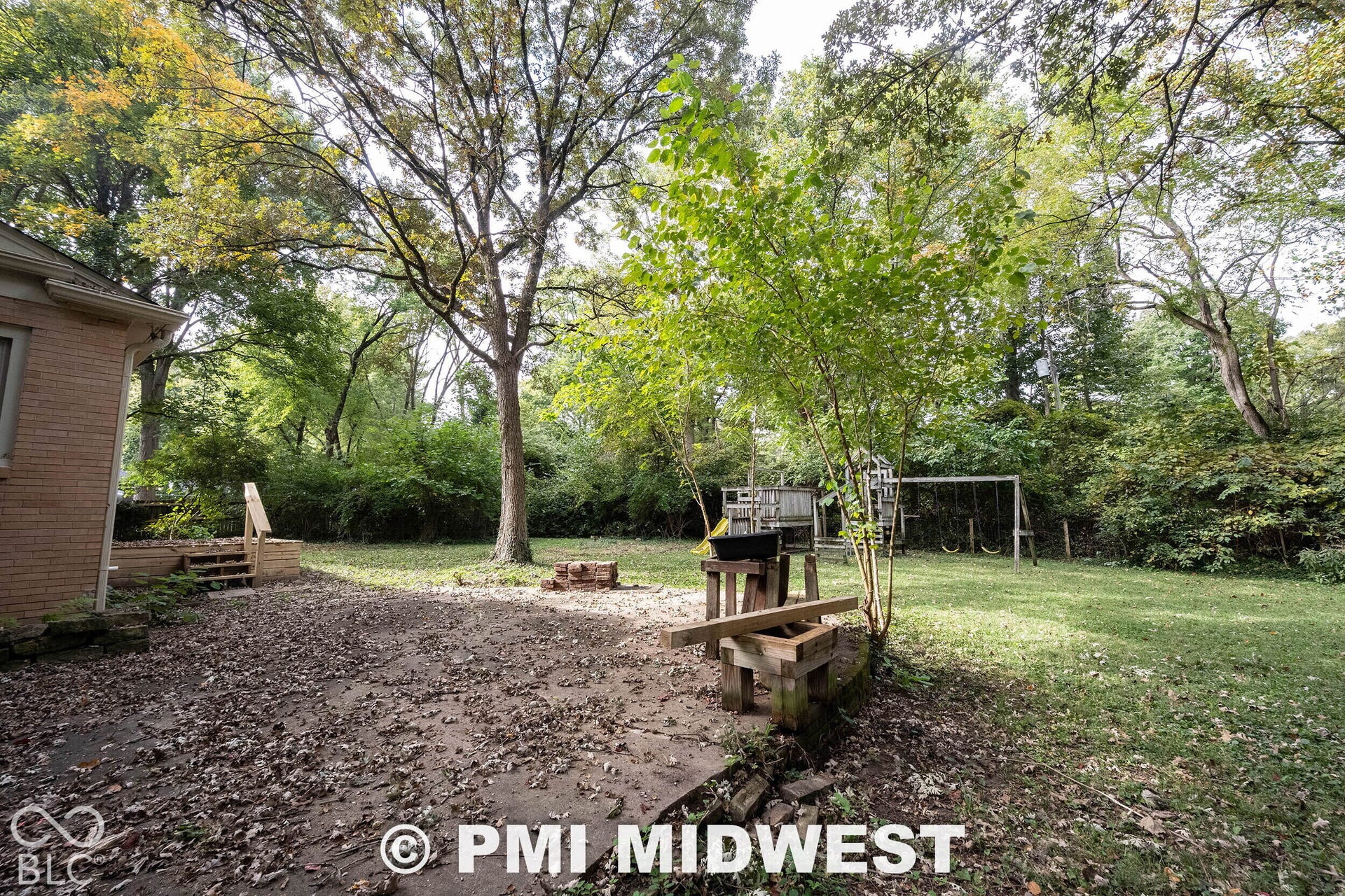 Expansive backyard featuring a concrete patio, wooden deck stairs, and mature trees