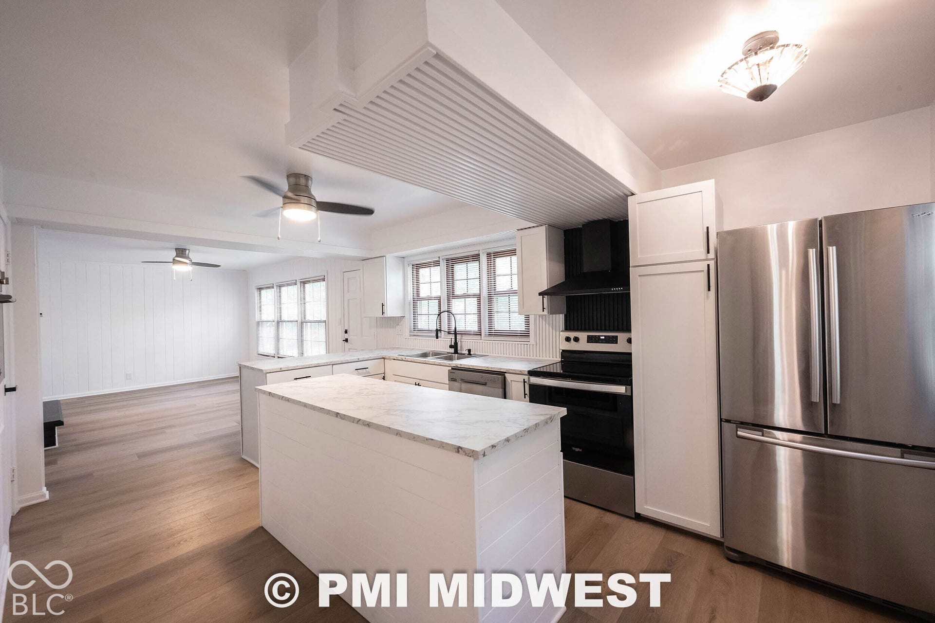 Kitchen featuring white cabinetry, an island with a stone-finish countertop, stainless steel appliances, wood-finish flooring, and a beadboard-paneled range hood surround