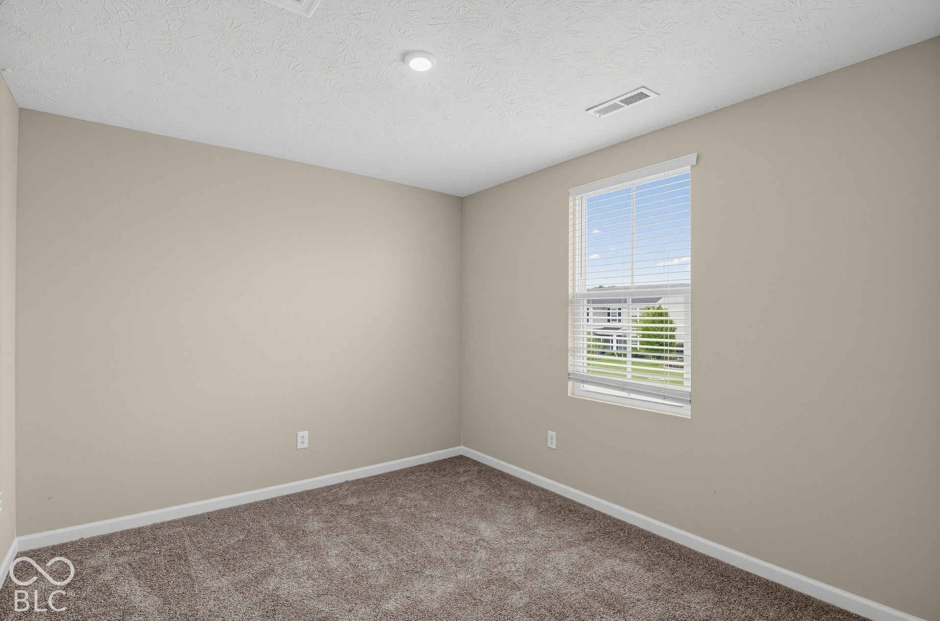Neutral interior space featuring neutral wall tones, textured carpeting, and a single-hung window with integrated blinds