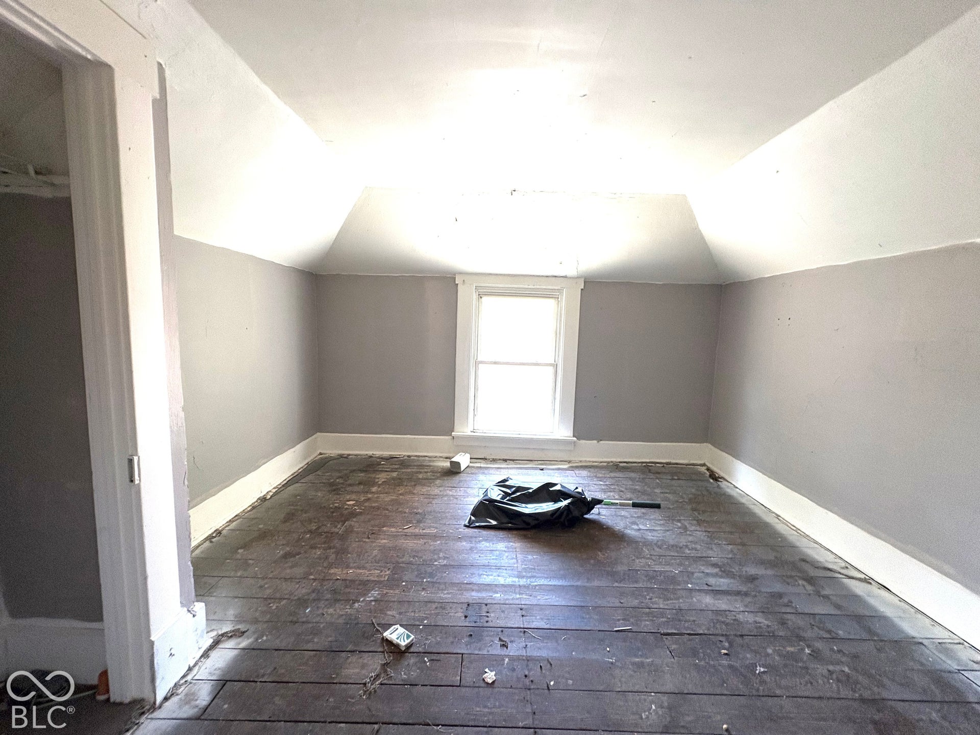 Interior space featuring vaulted ceilings, a central window with white millwork, and exposed wood plank flooring