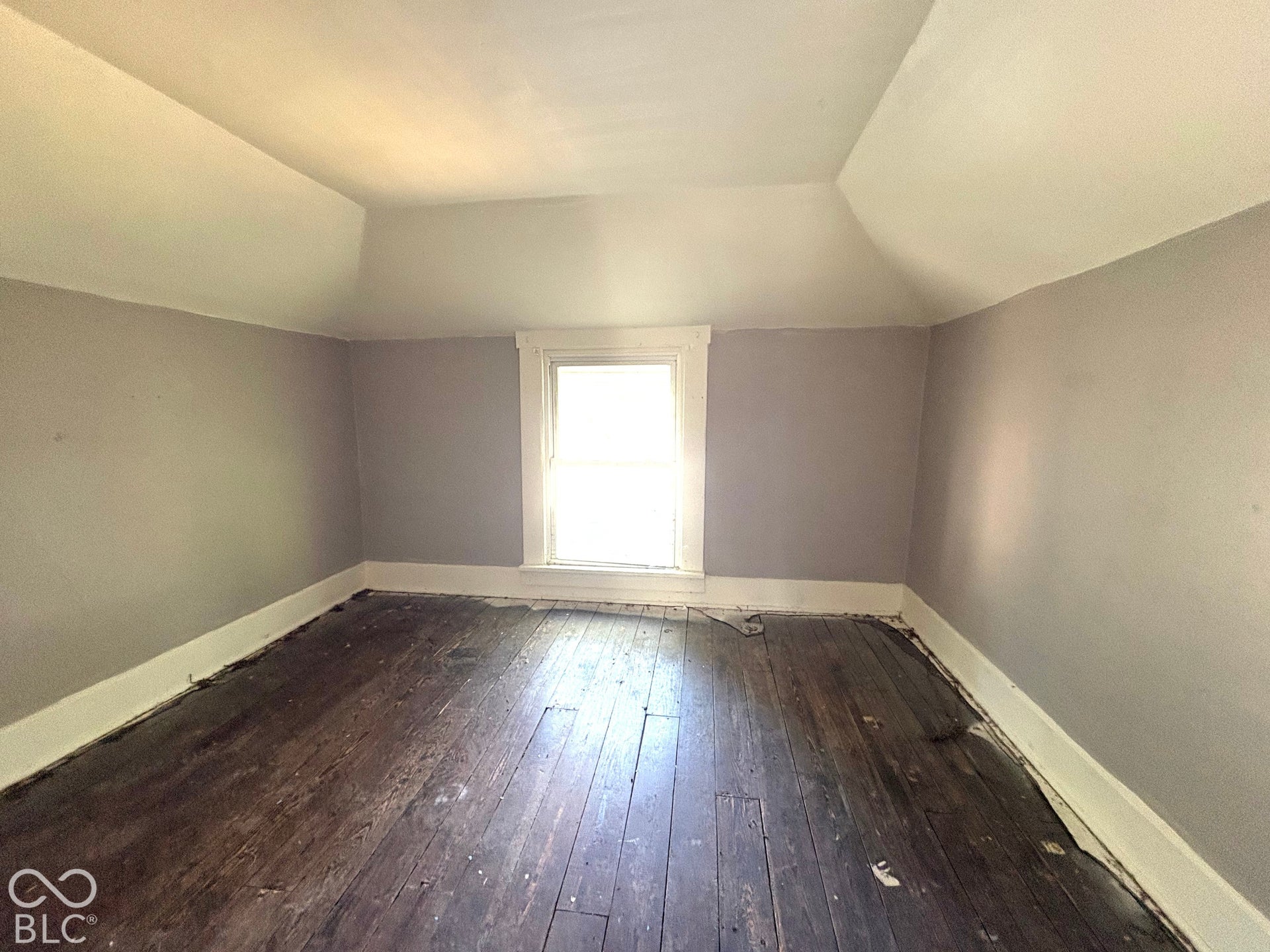 Interior room featuring vaulted ceilings, wide-plank wood flooring, and a single centered window with white casing