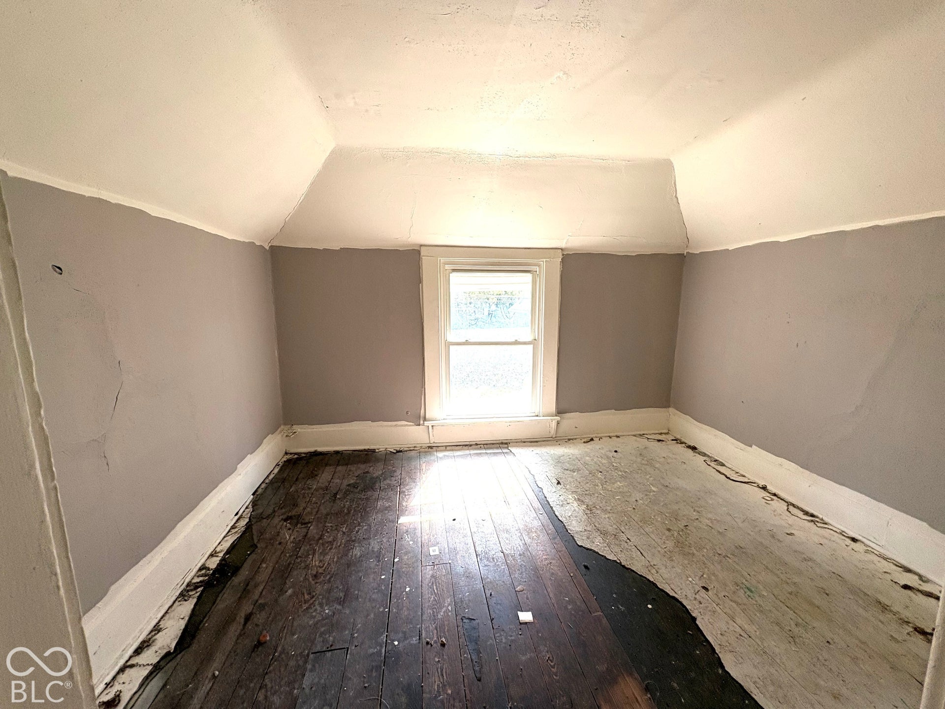 Room featuring slanted ceiling lines, wood-plank flooring, and a single centered window with white casing
