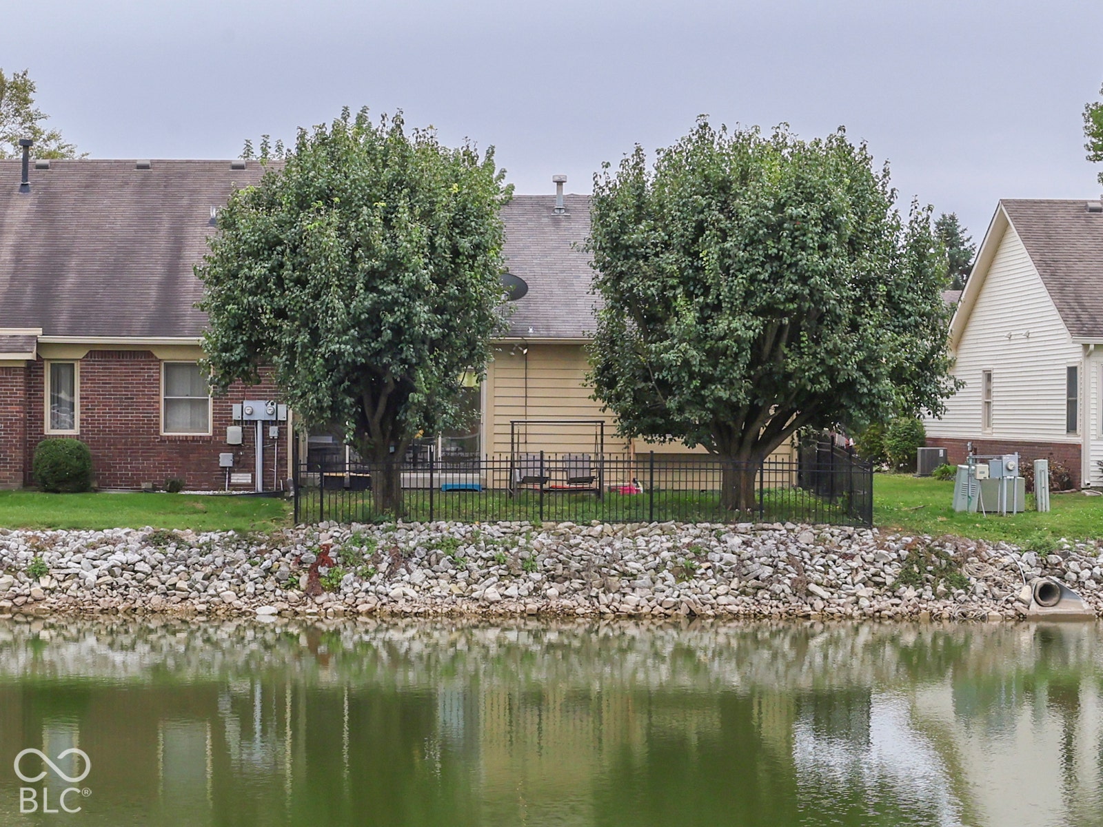 770 Ivy Lane, Greenwood, IN 46143 Waterfront property featuring a stone-lined bulkhead, a perimeter wrought iron fence, and mature ornamental trees