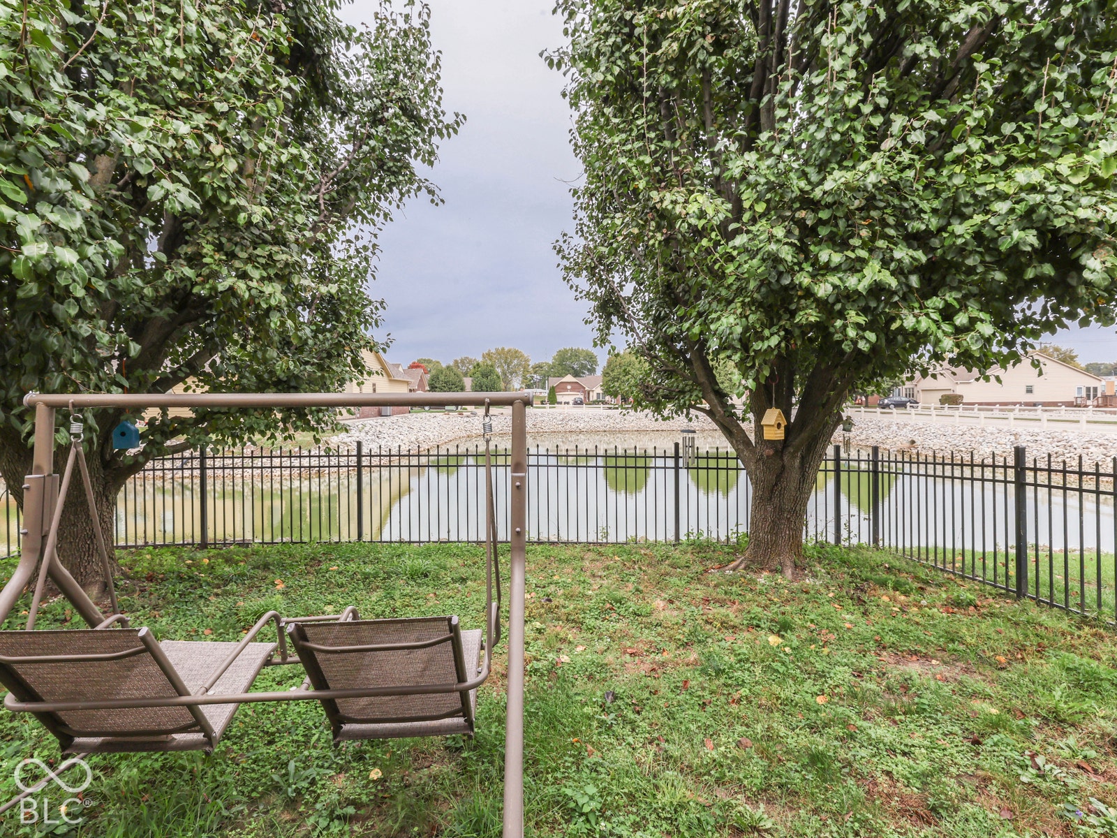 770 Ivy Lane, Greenwood, IN 46143 Waterfront backyard featuring mature shade trees, a stone-lined shoreline, and a metal perimeter fence