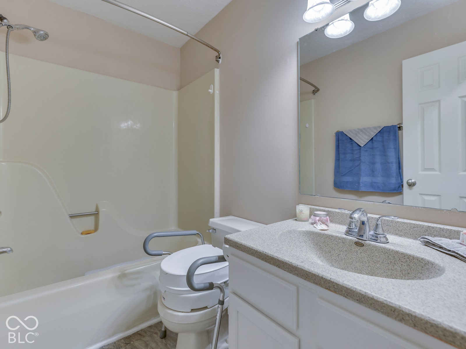 770 Ivy Lane, Greenwood, IN 46143 Bathroom featuring a vanity with a solid-surface integrated sink, molded tub surround, polished chrome faucet hardware, and a large-format vanity mirror with integrated multi-bulb lighting