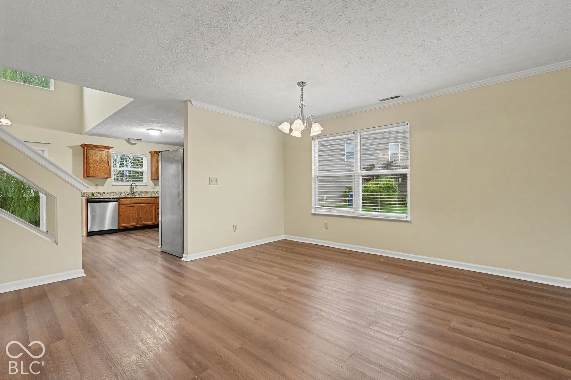 Open-concept area featuring wood-finish flooring, crown molding, multi-arm chandelier, and natural lighting provided by dual-pane windows