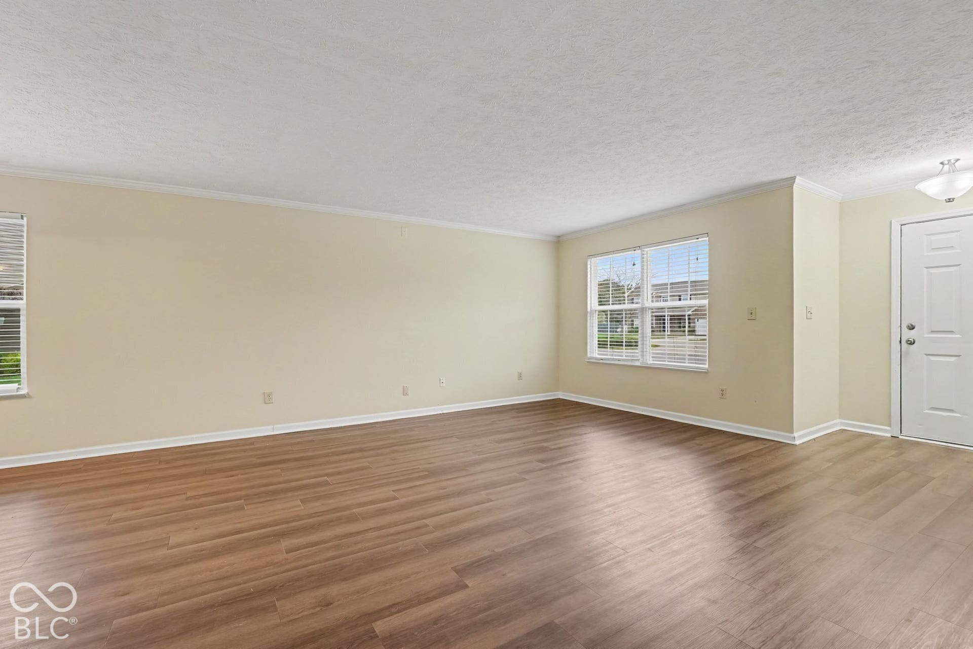 Open-concept interior featuring wood-finish flooring, neutral wall paint, multi-pane windows, and a flush-mount ceiling light fixture