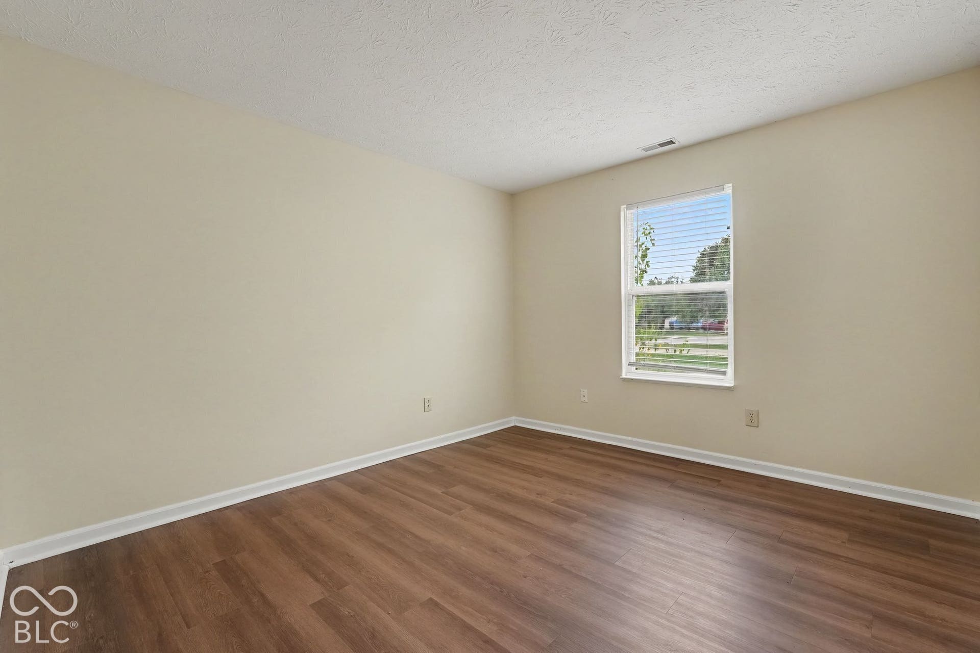 Neutral interior space featuring wood-finish flooring, a single-hung window with blinds, and painted walls