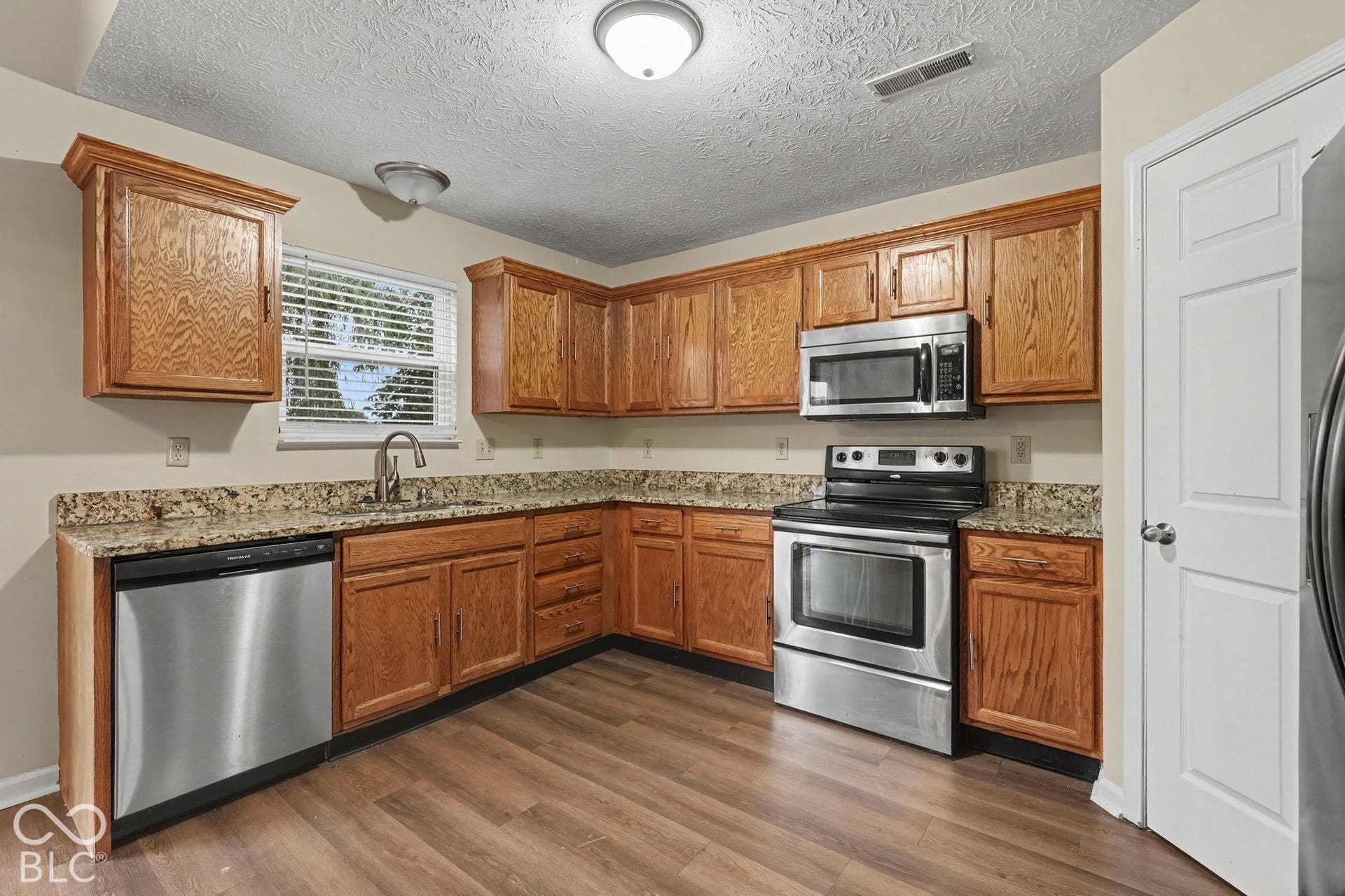 Kitchen featuring stained wood cabinetry, stone-surface countertops, wood-finish flooring, and stainless steel appliances including a built-in microwave, range, and dishwasher