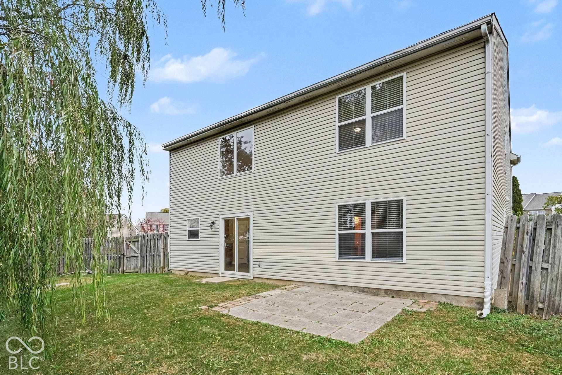 Two-story residence exterior featuring horizontal siding, a rear stone-paver patio, sliding glass doors, and a wood privacy fence