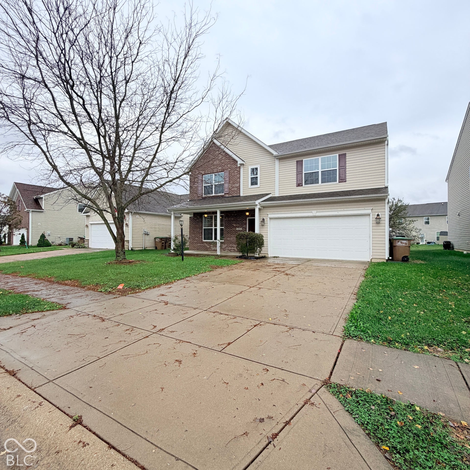 Two-story residence featuring light-colored vinyl siding, partial brick facade, attached two-car garage, and a concrete driveway
