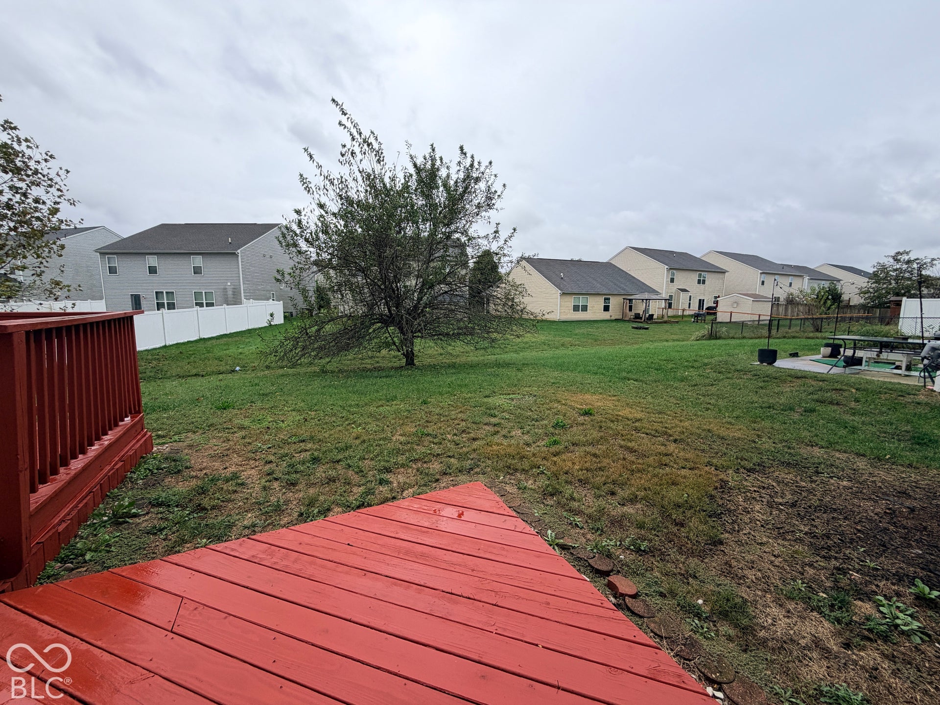 Rear wooden deck featuring a painted finish and railing, opening to a grass yard with a perimeter white vinyl privacy fence