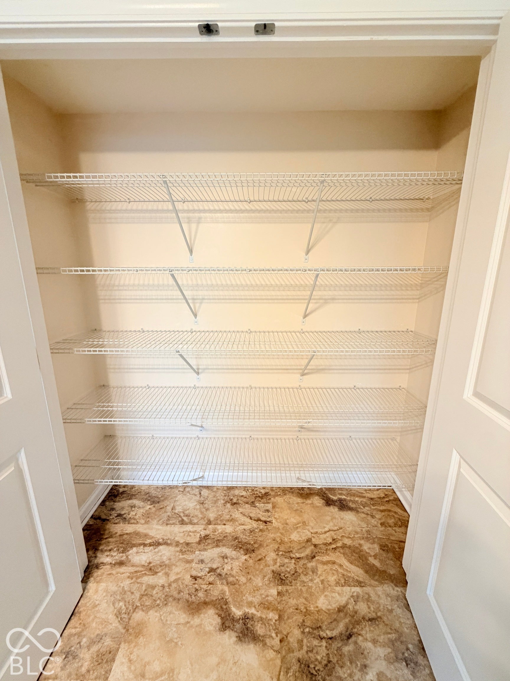 Storage area featuring five tiers of white wire shelving and patterned floor tiling