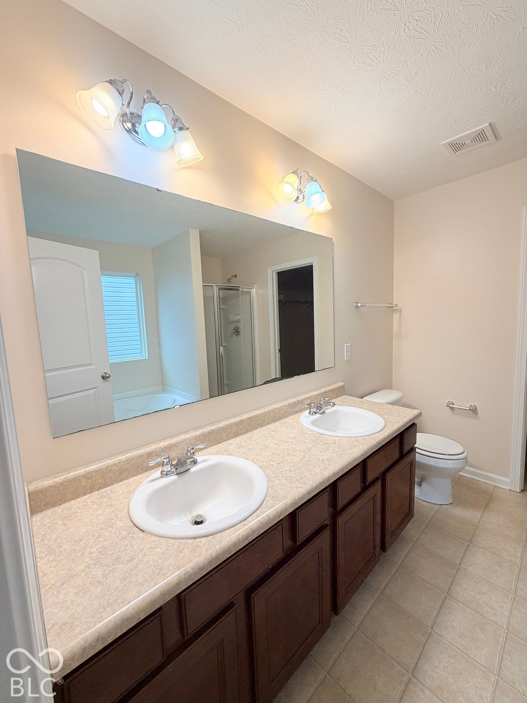 Dual-sink vanity with stone-finish countertop, dark wood-finish cabinetry, full-width wall mirror, and dual multi-light fixtures